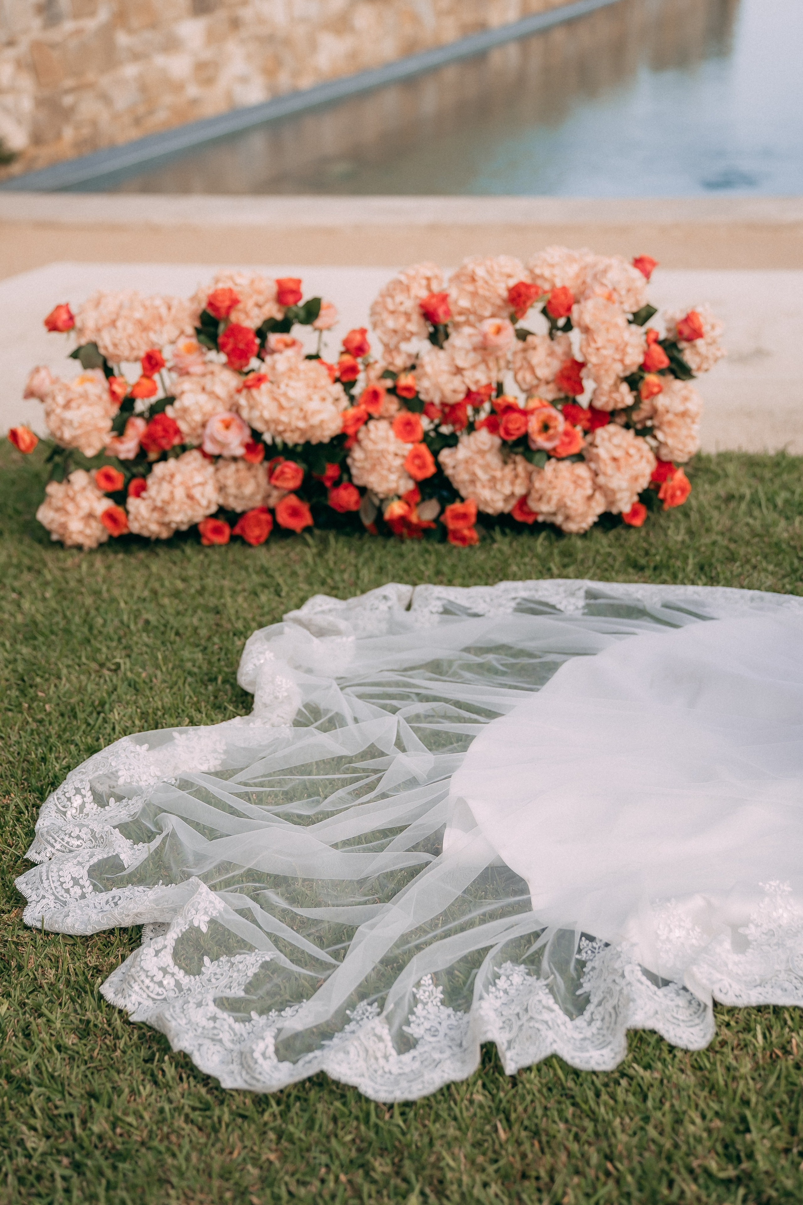 Bride's lace veil spread on the grass beside the red floral arrangement