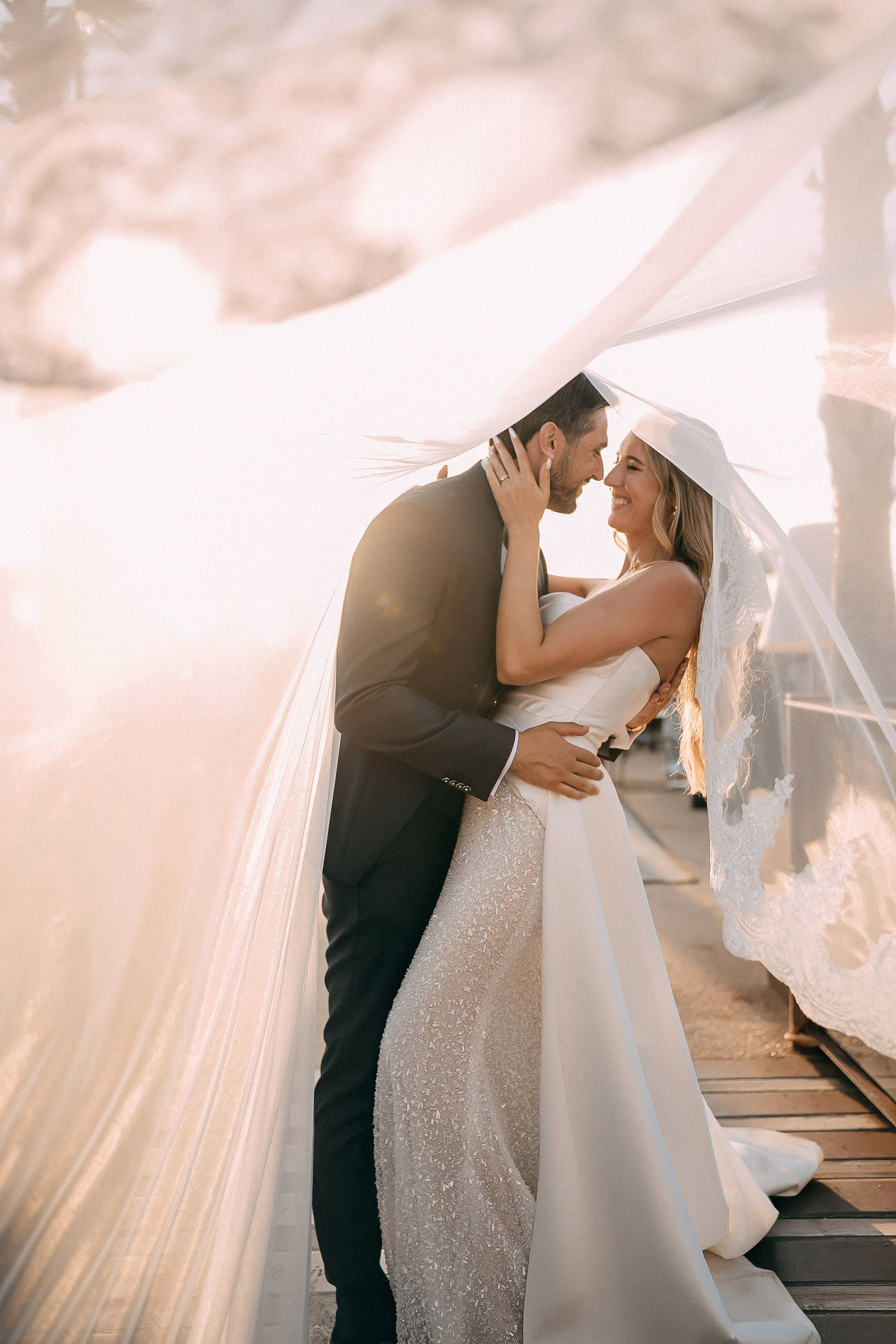 Bride and groom kissing under the veil in golden evening light
