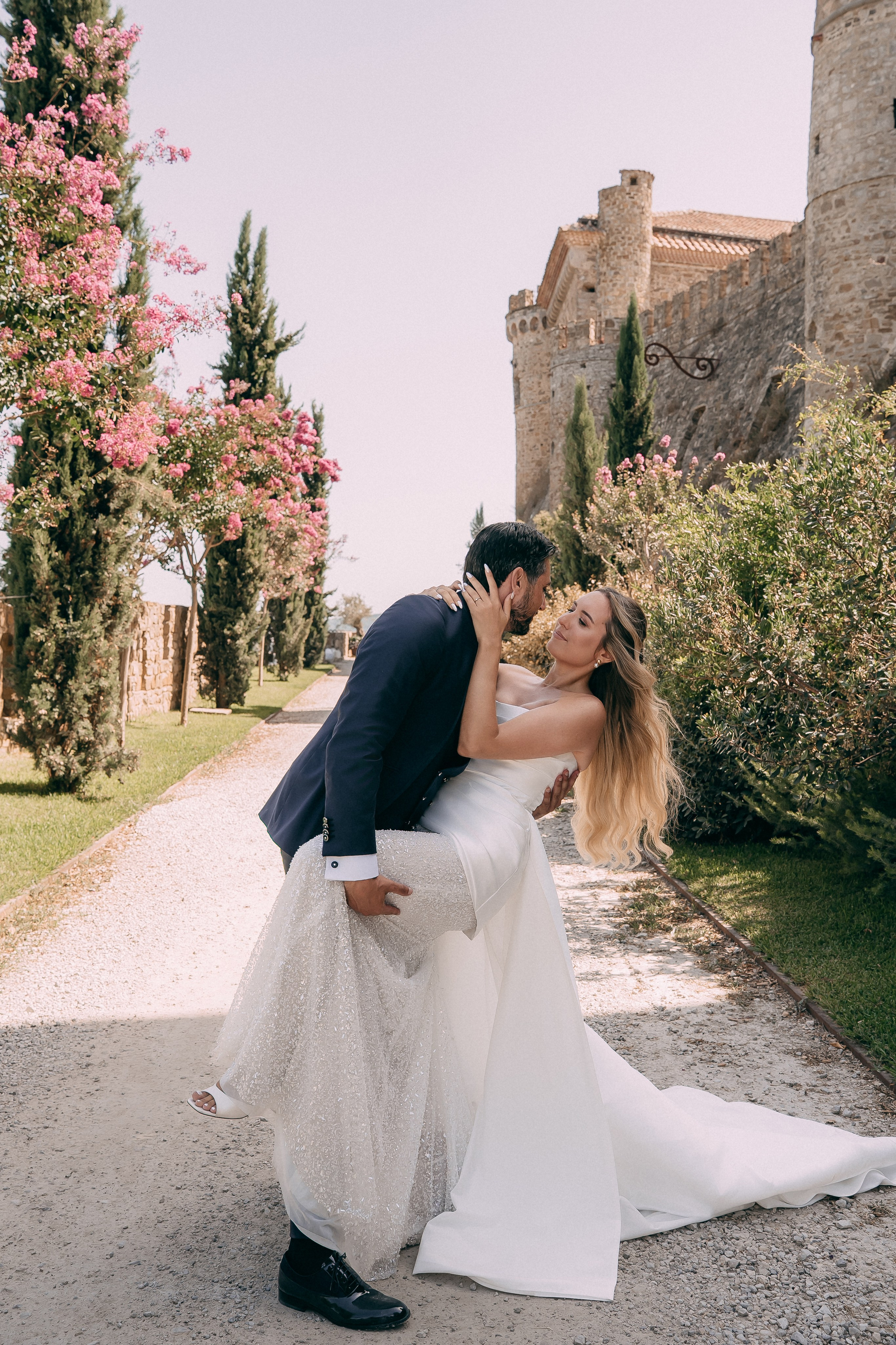 Groom lifting the bride on the flower-lined path at the castle