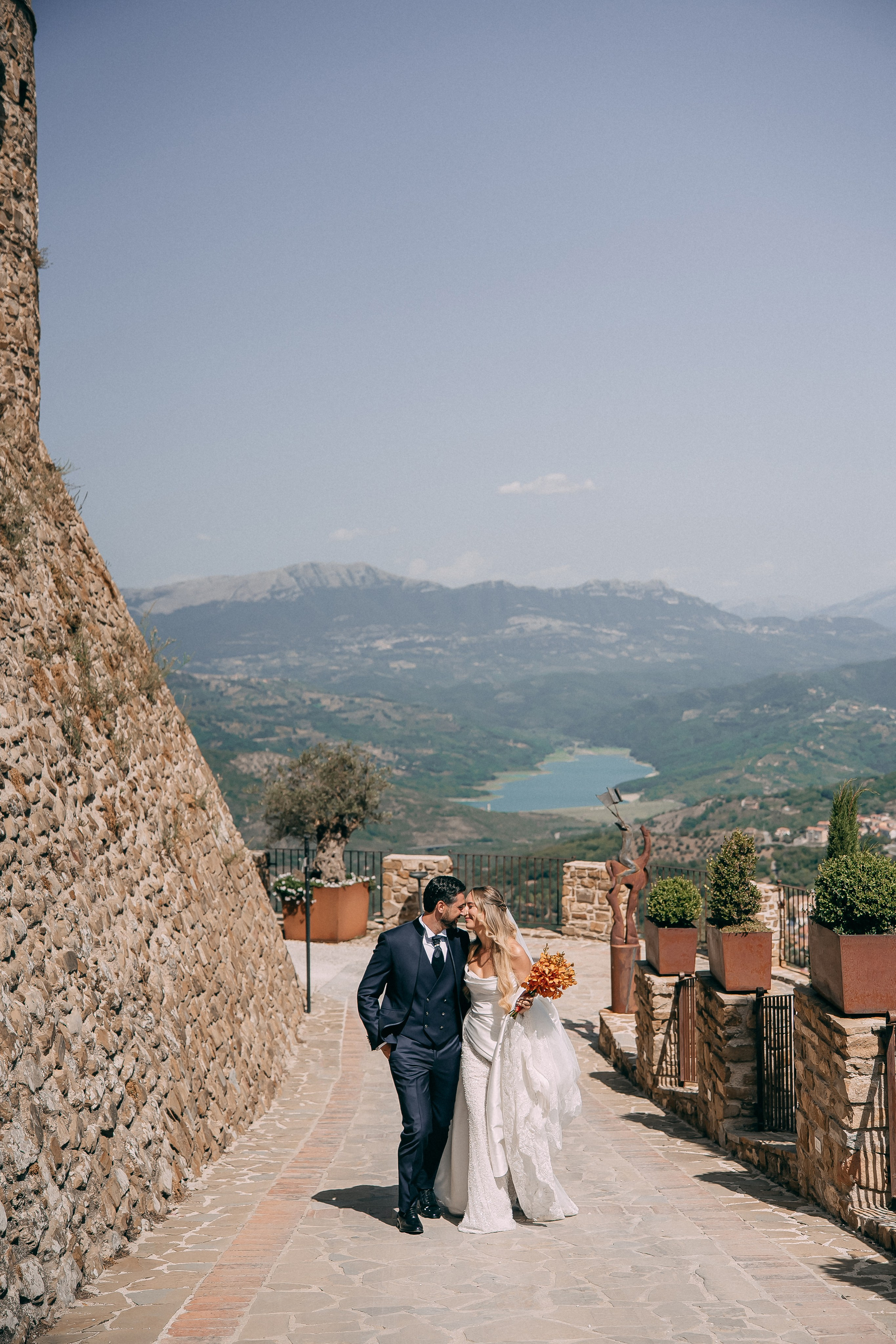 Newlyweds kissing on the stone path above the valley at Rocca Cilento