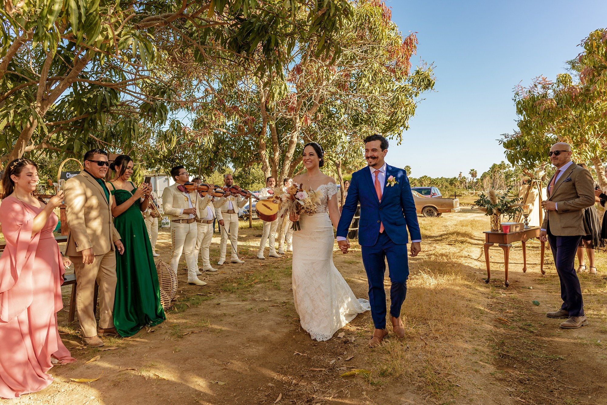 Outdoor wedding reception in Los Cabos – newlyweds entrance with mariachis and guests, vibrant Mexican destination wedding celebration
