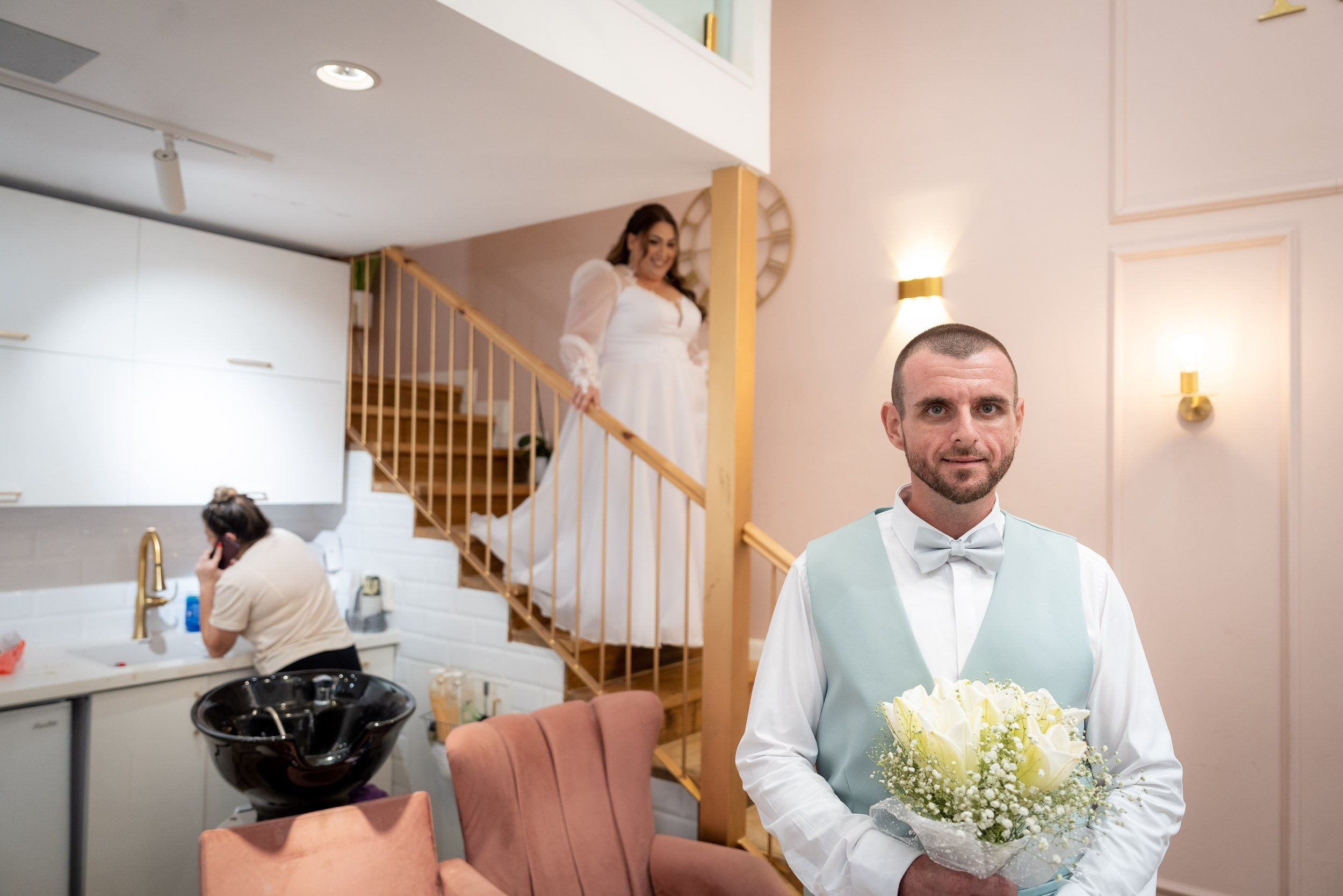 Matan holds the bouquet as Ella walks down the stairs towards him
