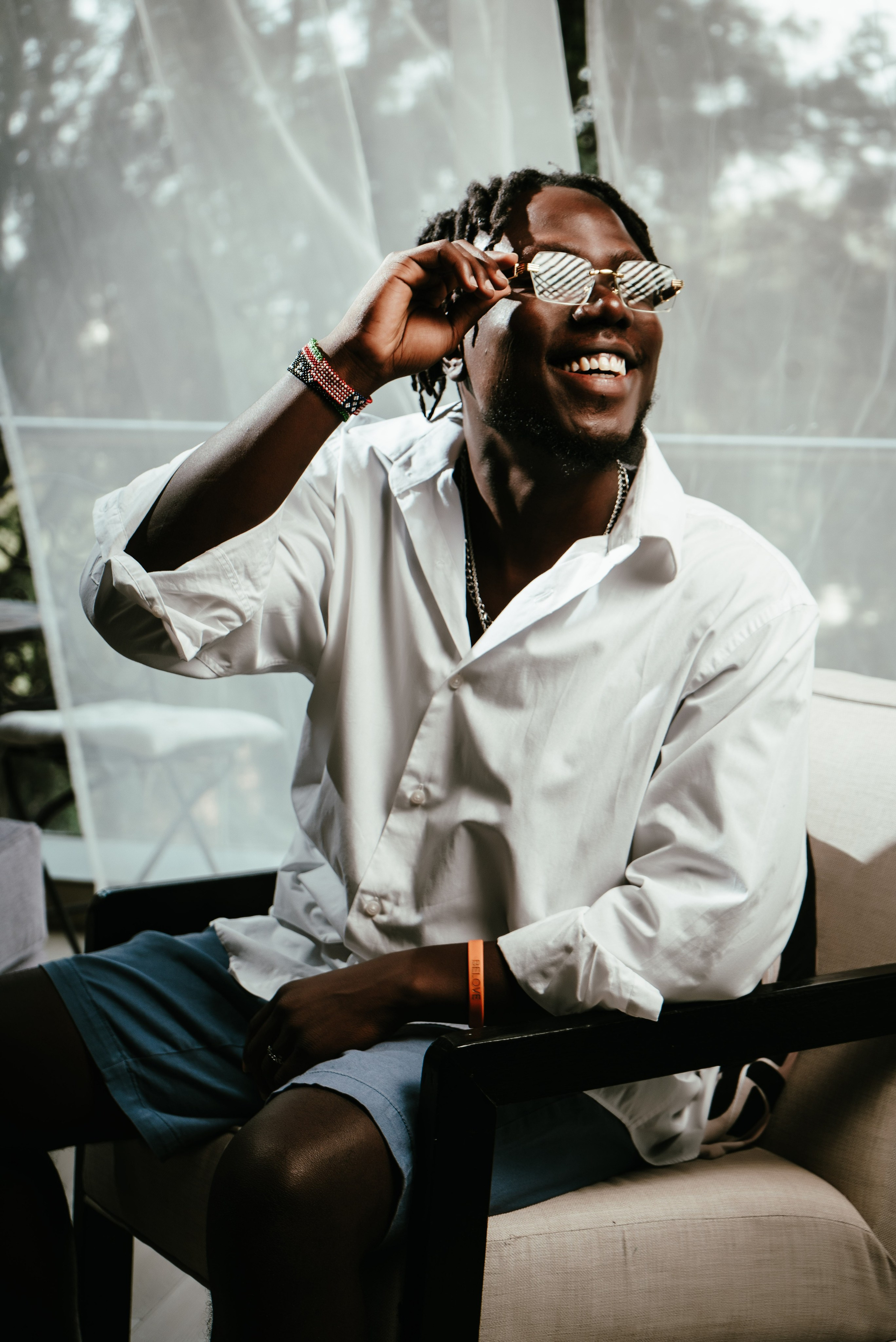 Man in white shirt smiling and adjusting sunglasses — lifestyle portrait by Nick Ouma Photography, Nairobi