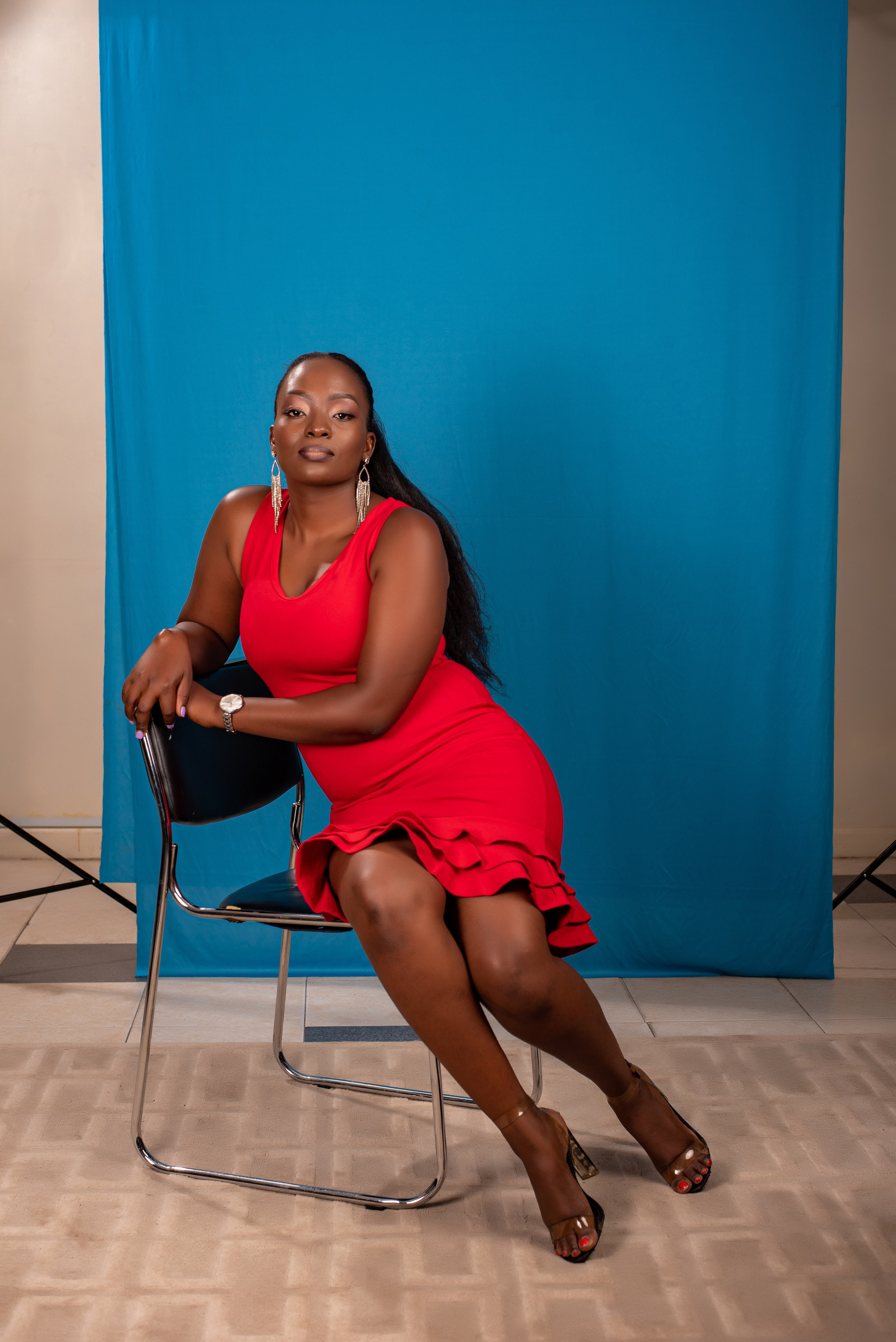 Woman in red dress seated against blue backdrop — bold studio portrait by Nick Ouma Photography, Kenya