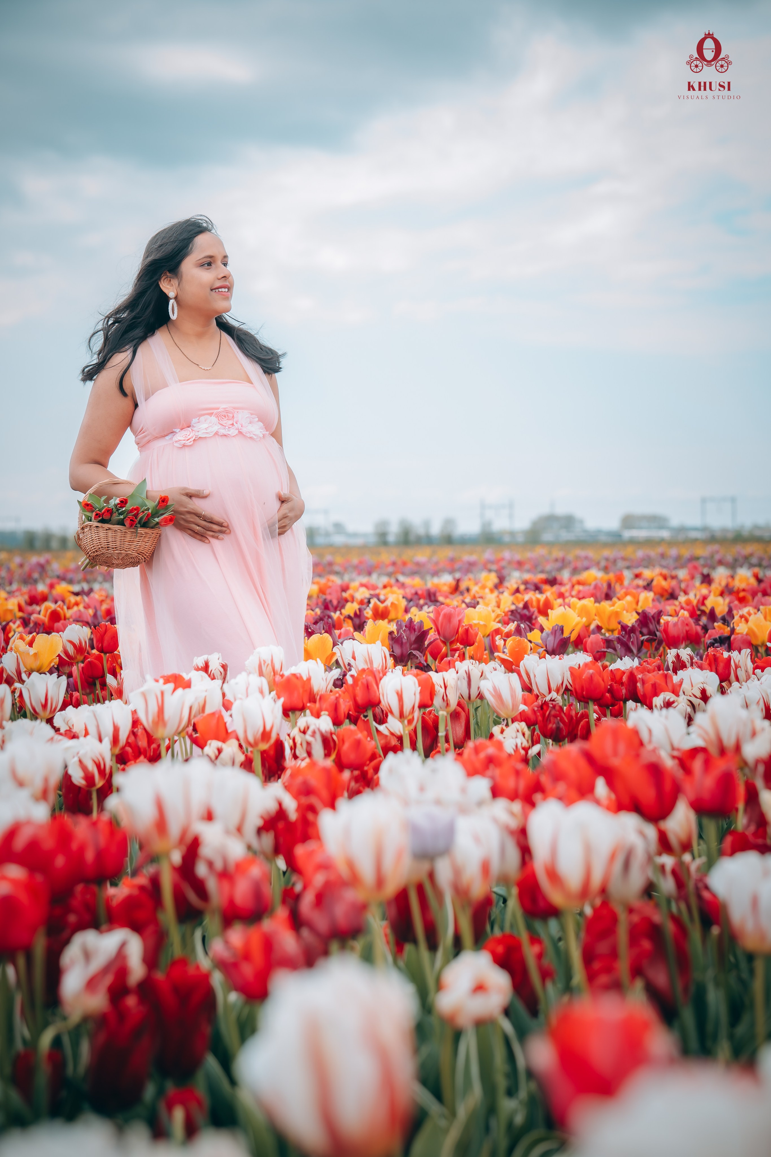 A pregnant woman standing in a white red tulip field in Netherlands holding a tulip flower basket