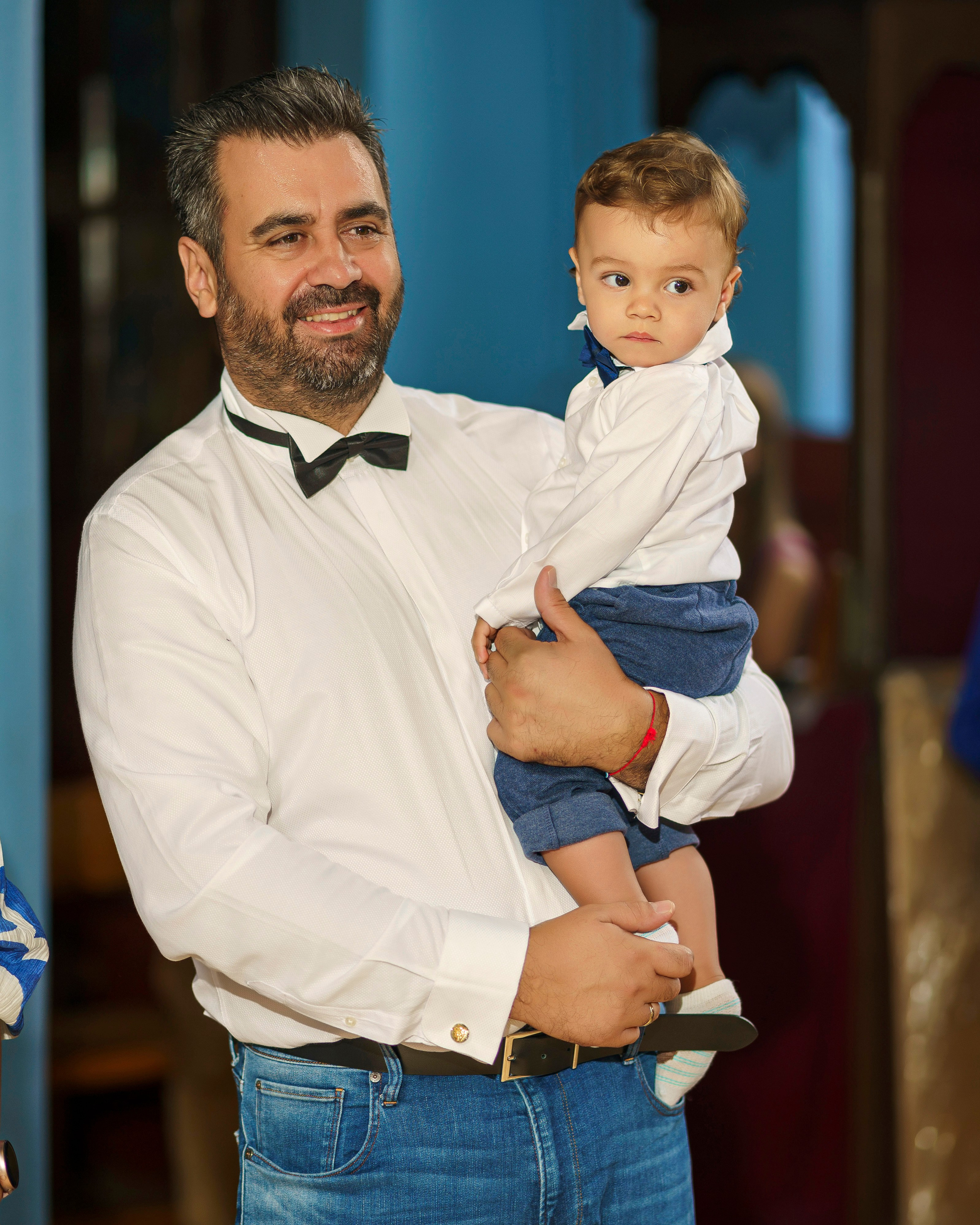 Баща с официално облекло държи бебе в църква по време на тържеството за Свето кръщение.