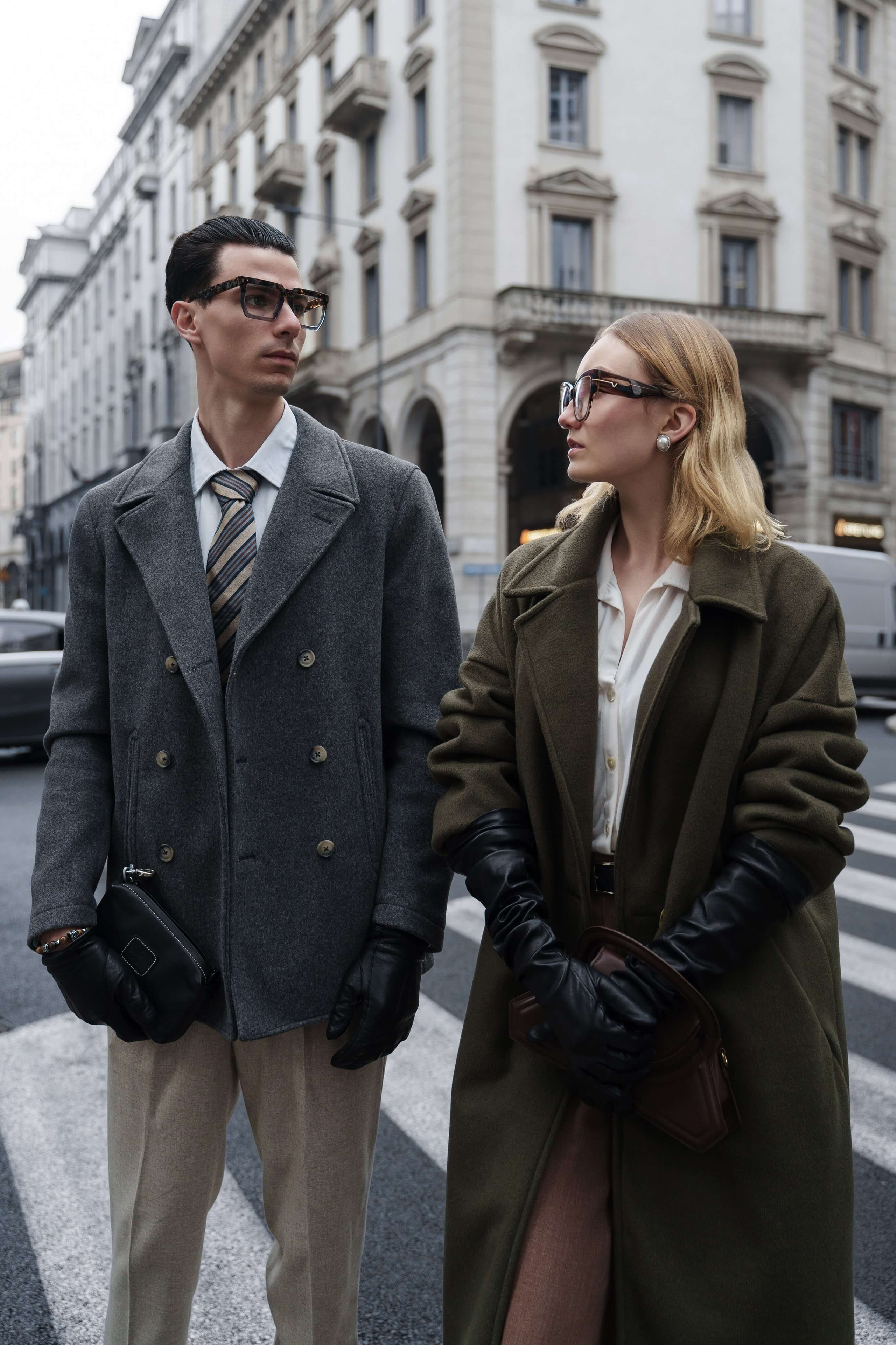 Stylish couple standing on a zebra crossing in Milan wearing sunglasses and tailored coats