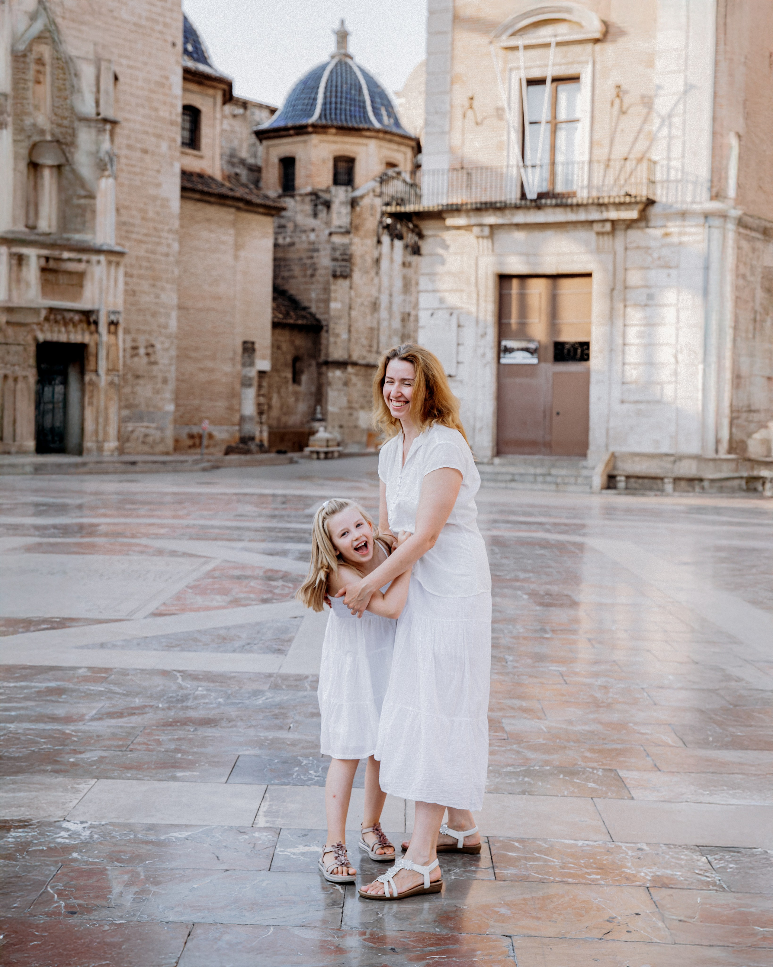 Madre e hija compartiendo un momento alegre frente a arquitectura histórica en Valencia, España — captura espontánea ideal para sesiones familiares atemporales en Valencia y España.