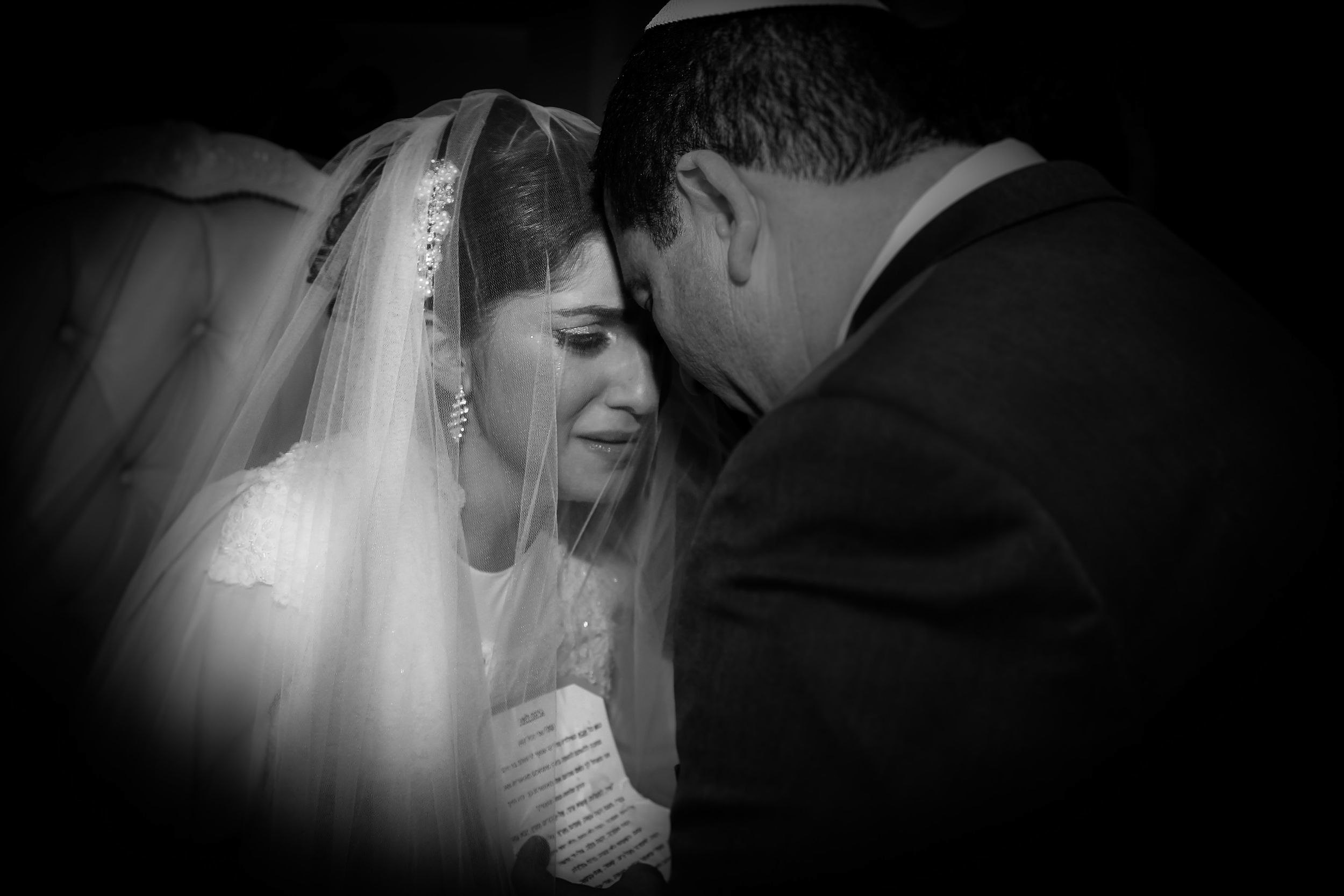 A tearful bride rests her forehead against her father during the bedeken ceremony