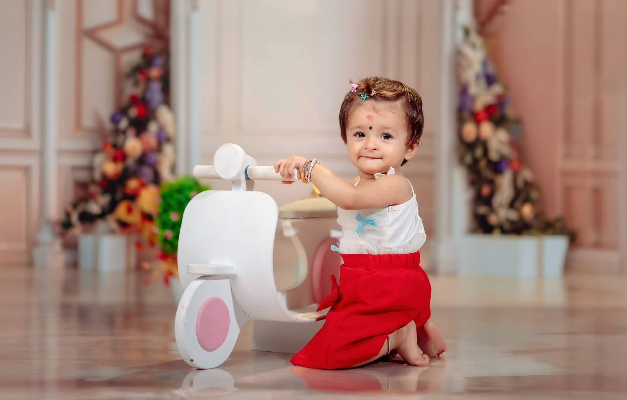 A toddler posing next to a vintage white toy scooter during a birthday photoshoot in Nepal.