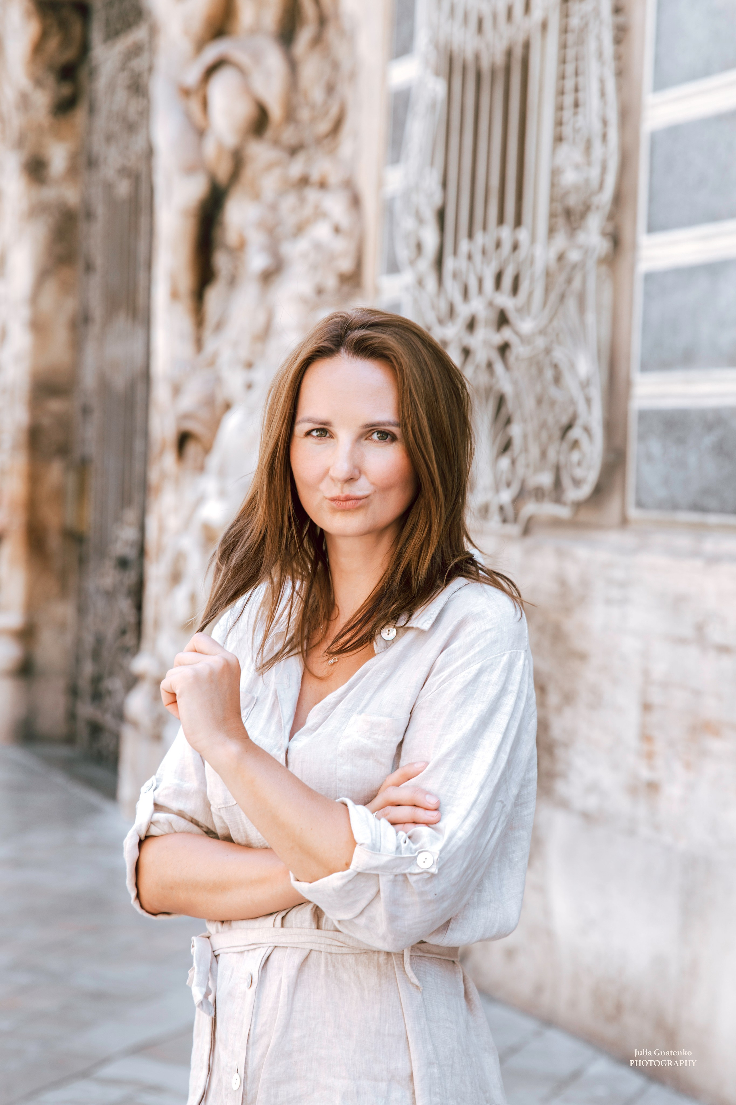 Портрет женщины в легком льняном платье, уверенно стоящей перед изысканным барочным зданием с декоративными коваными элементами в Валенсии, Испания