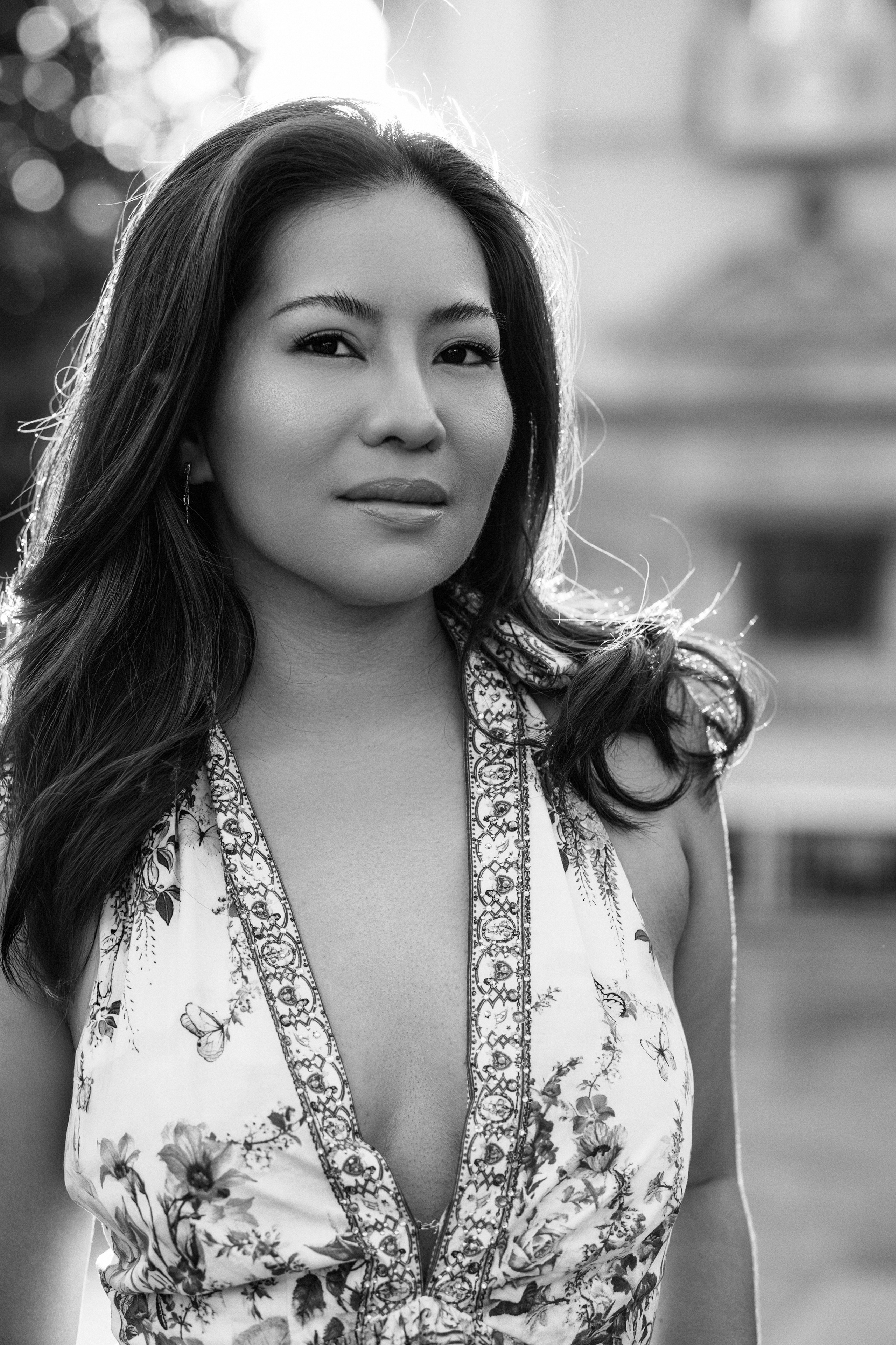 Sesión de retrato femenino en Valencia, España, con una mujer vestida con un vestido floral de verano en un retrato atemporal en blanco y negro. Fotografiada con suave luz natural y un fondo urbano desenfocado, esta elegante y expresiva imagen resalta la confianza, la belleza y las emociones auténticas, ideal para fotografía de retrato femenino, sesiones individuales, marca personal, retratos lifestyle y fotografía profesional de retrato en Valencia y toda España.
