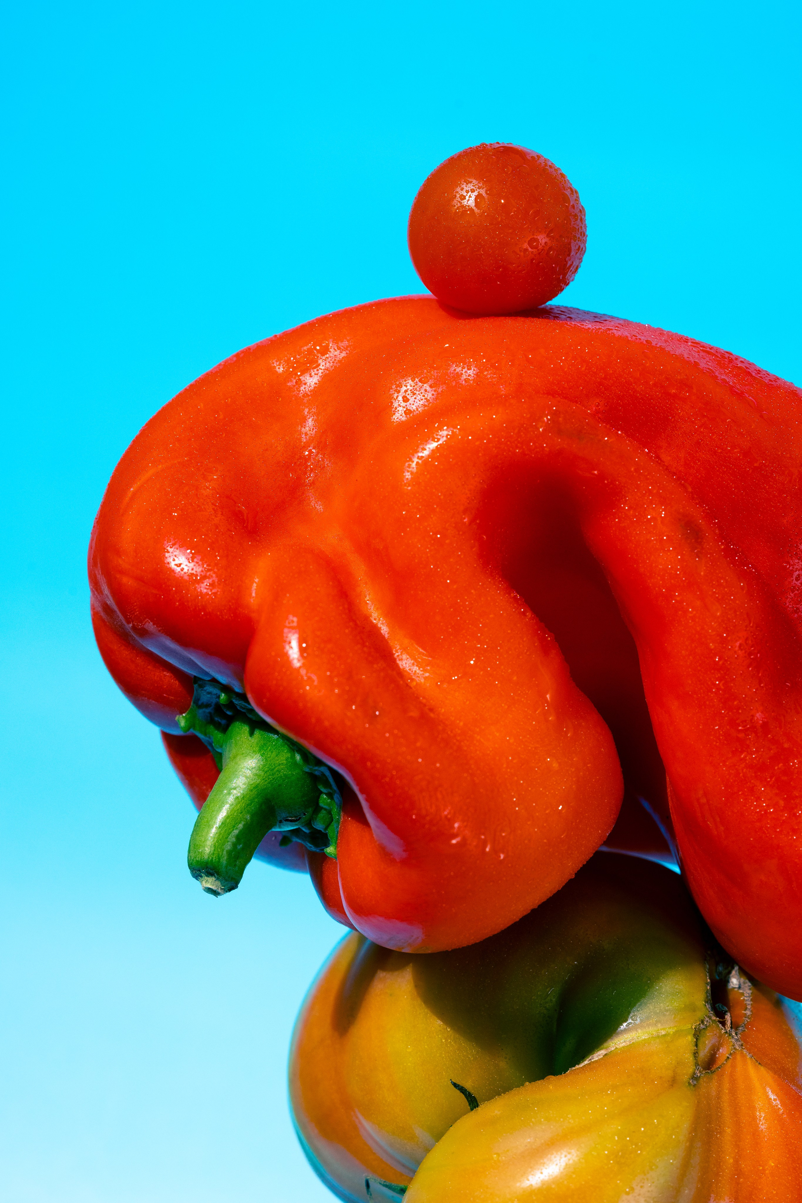 Яркий крупный план красного перца и помидора на синем фоне. Композиция крупным планом из красного перца, томатов-реликвий и помидора черри, сложенных друг на друга на ярко-синем фоне.