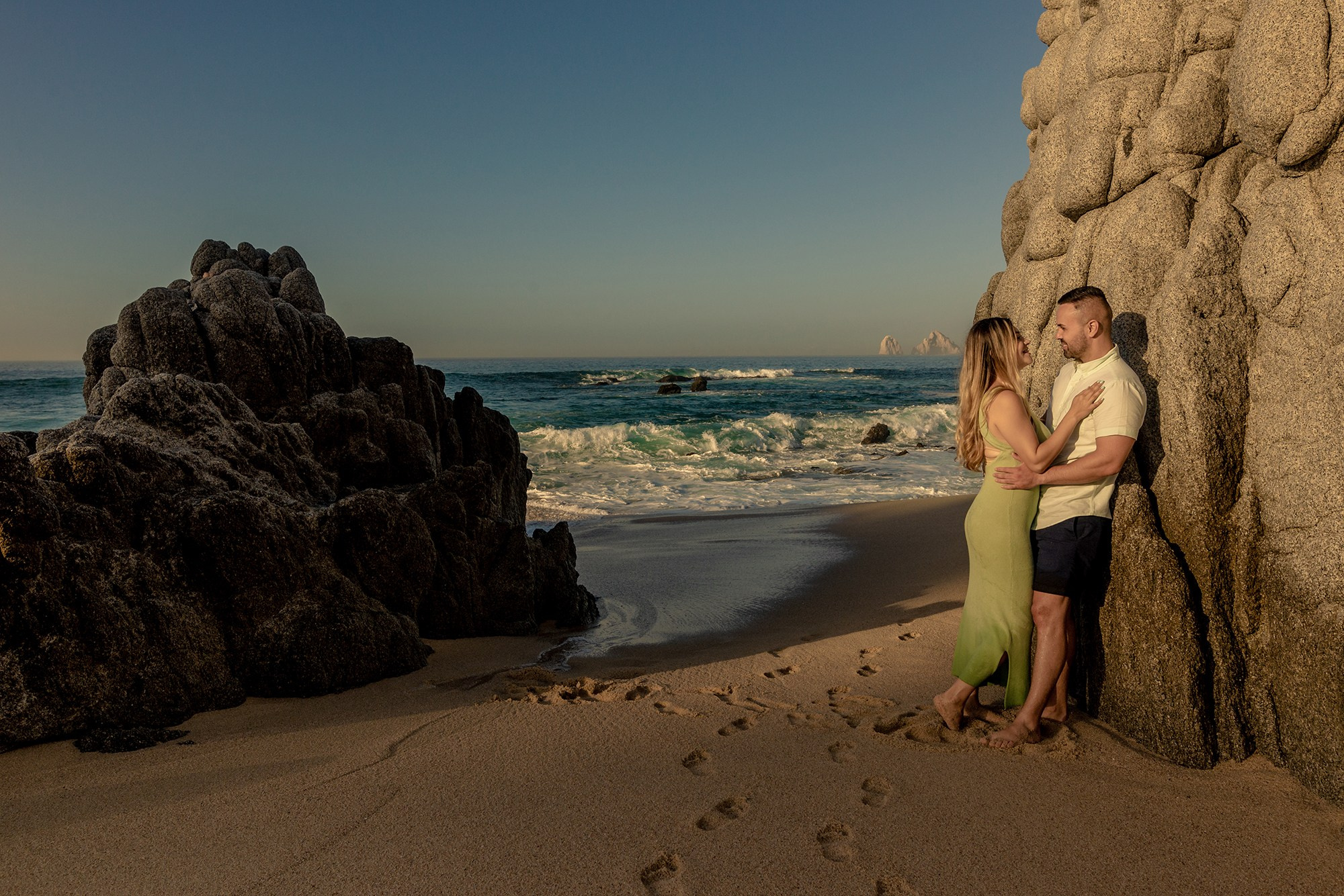 Sunset couple portrait in Cabo San Lucas – romantic embrace framed by rocks with the iconic Arch in background