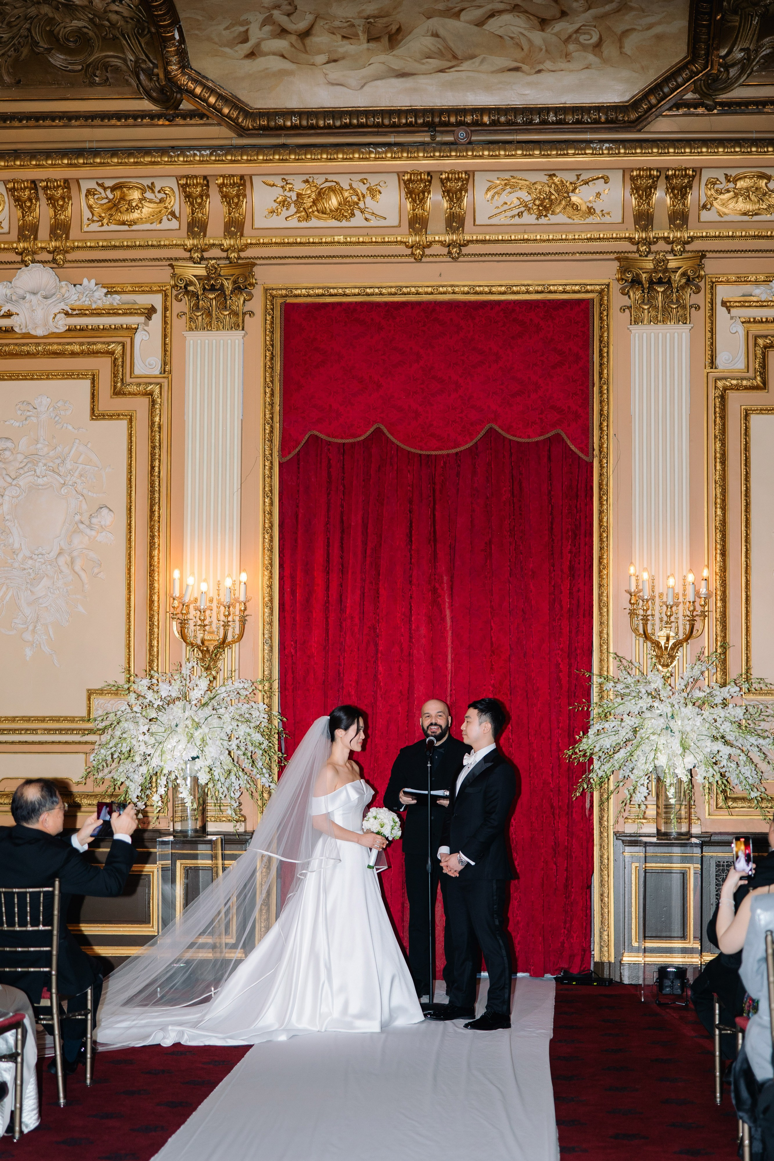 a bride and groom are standing in front of a red curtain