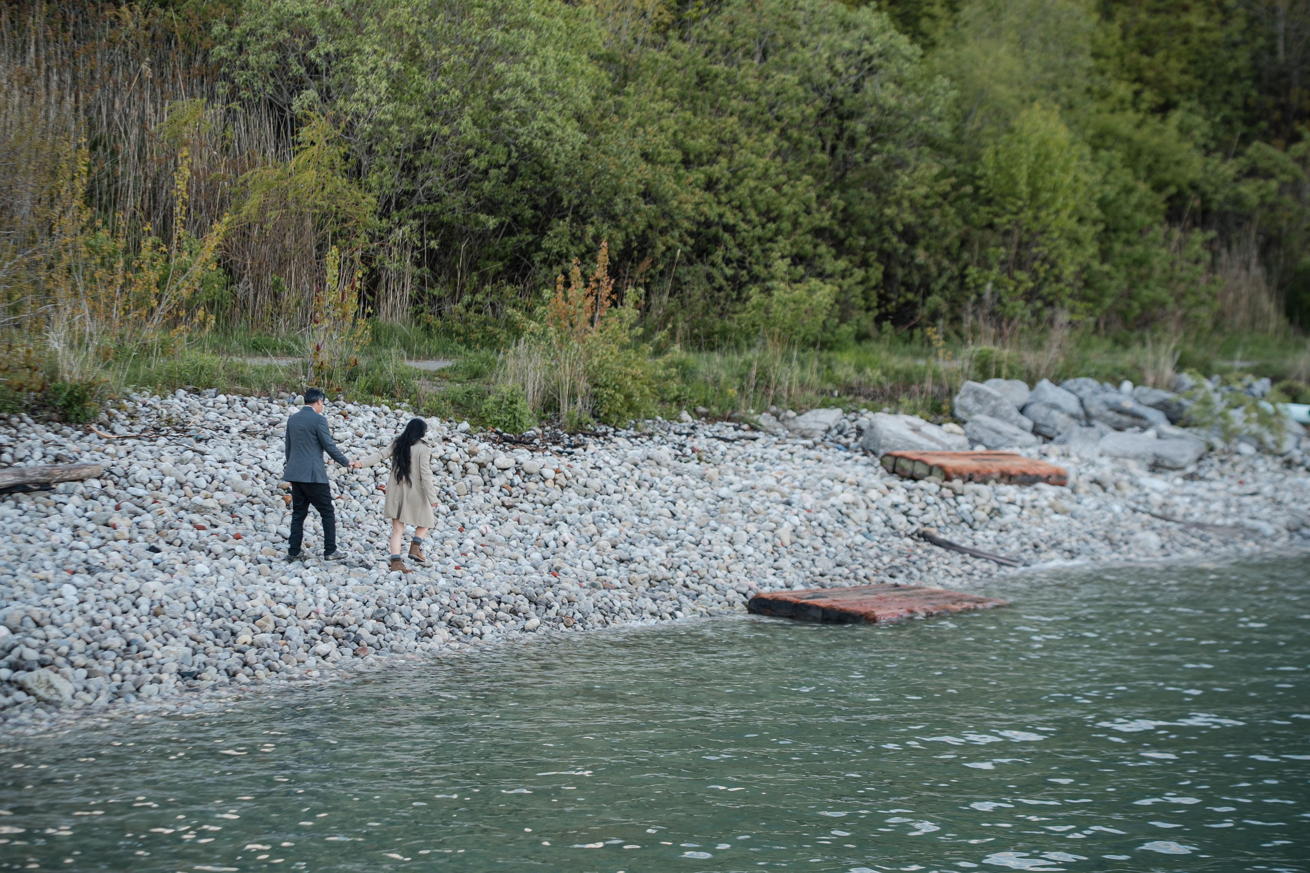 Couple walking hand in hand on a wooden boardwalk by the lake during their engagement photoshoot.
