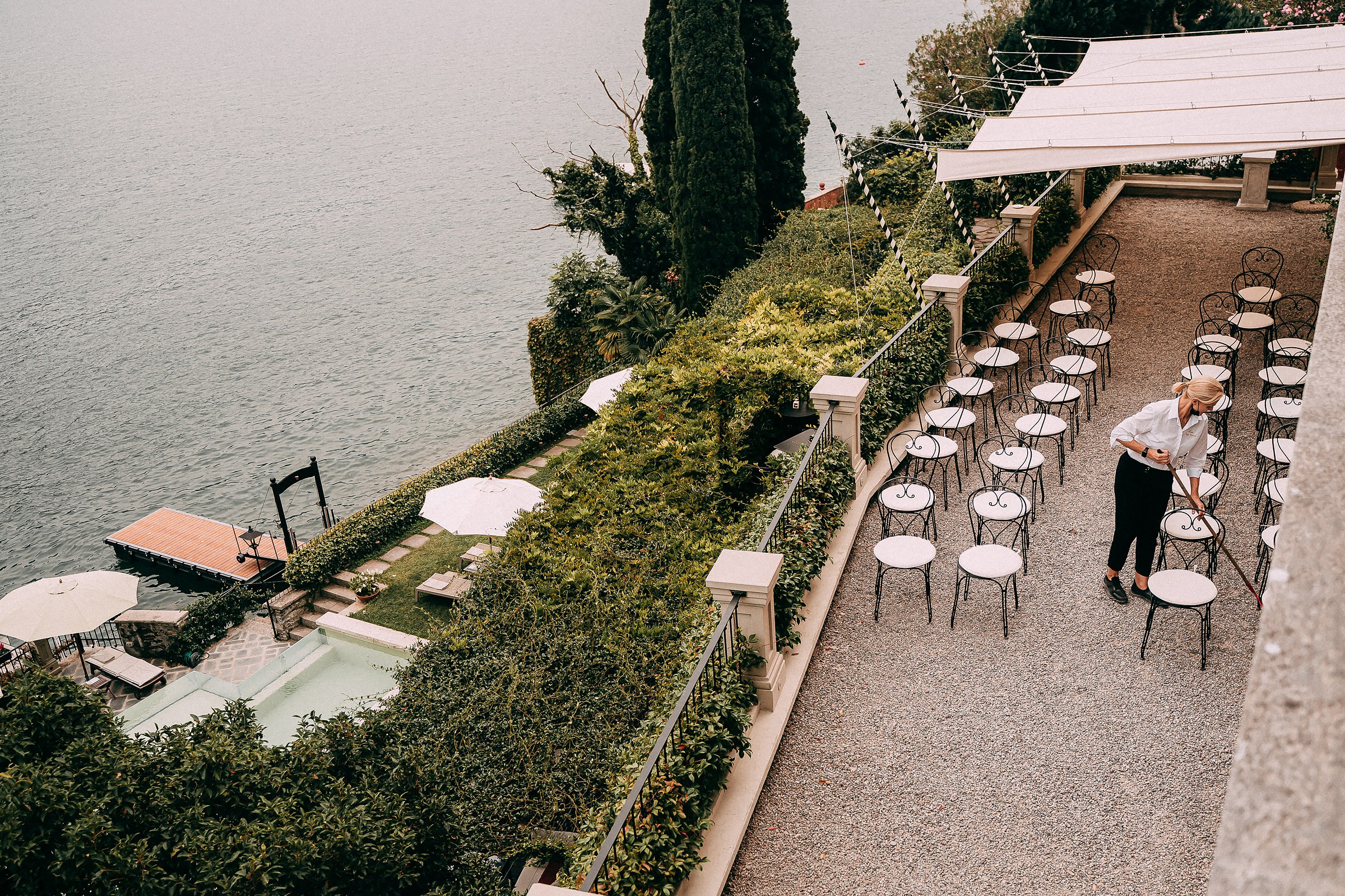 Lakeside terrace of Villa Vittoria arranged for an event with rows of white chairs facing the water. A pool area below features umbrellas and lounge chairs surrounded by greenery.