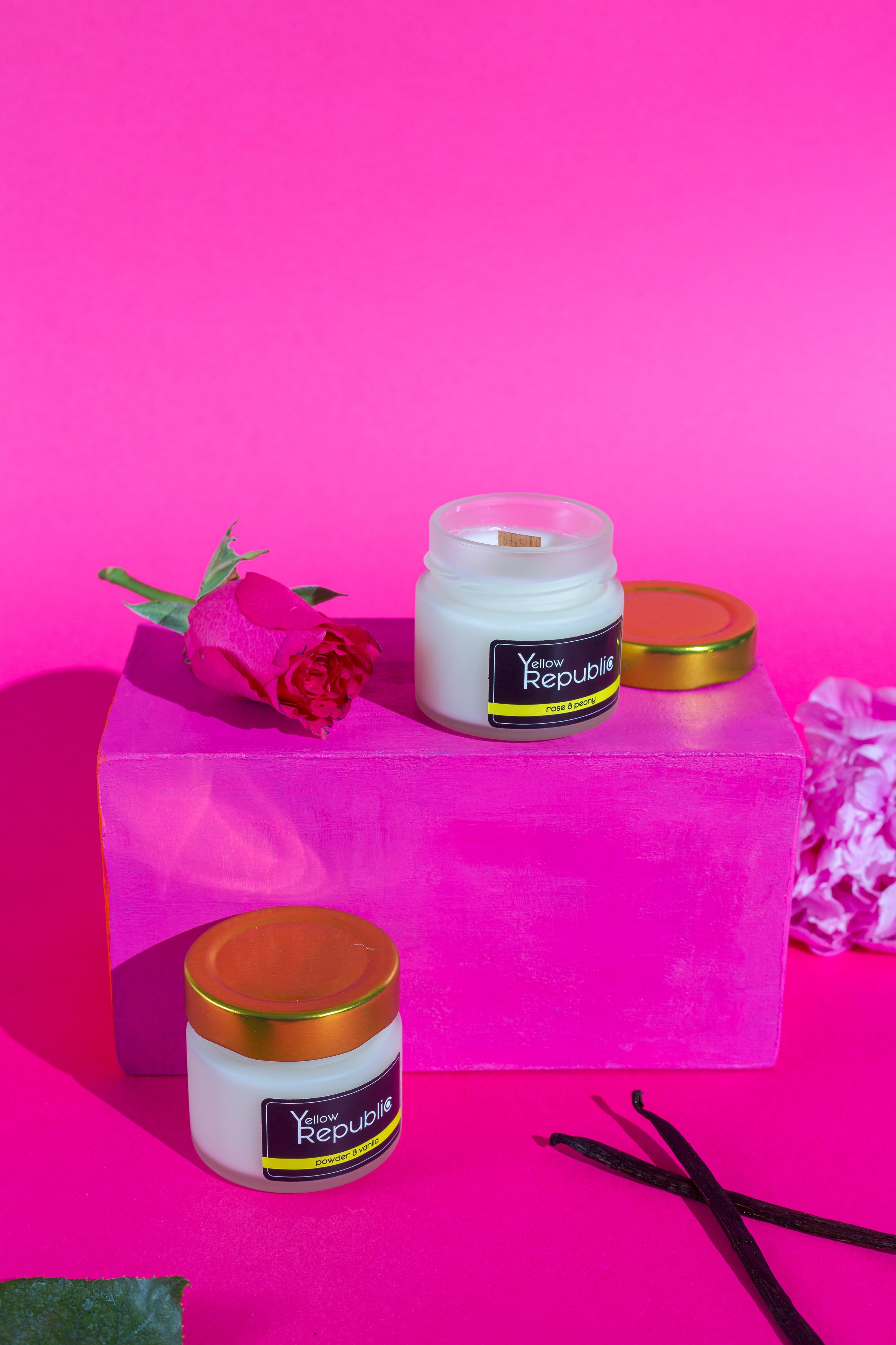 Velas con aroma a vainilla sobre fondo rosa con rosas y vainas de vainilla