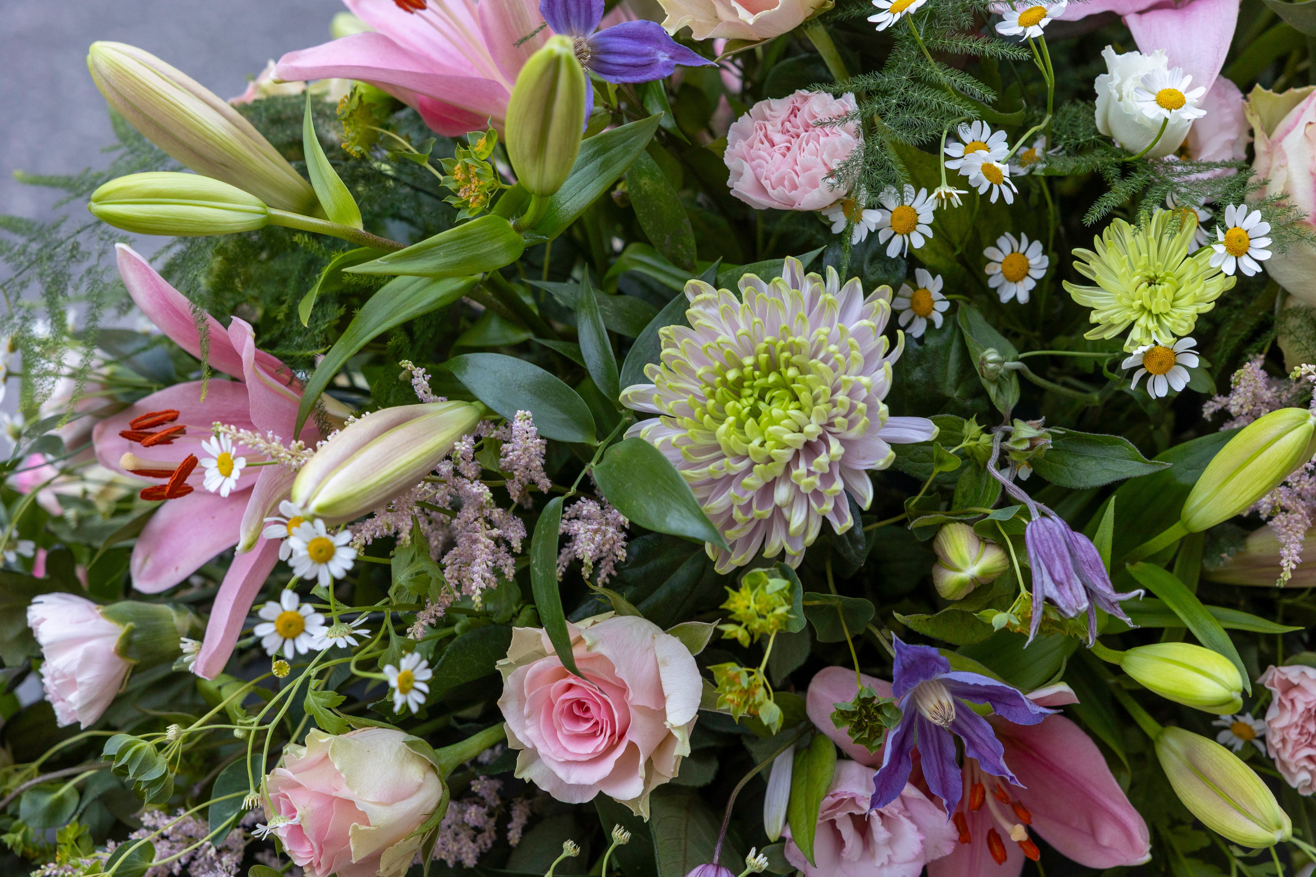 Smuk kistepynt med lyserøde blomster, grønt og naturlige detaljer. En elegant blomsterdekoration fra Akropolis Blomster, der udtrykker kærlighed, taknemmelighed og varme minder.