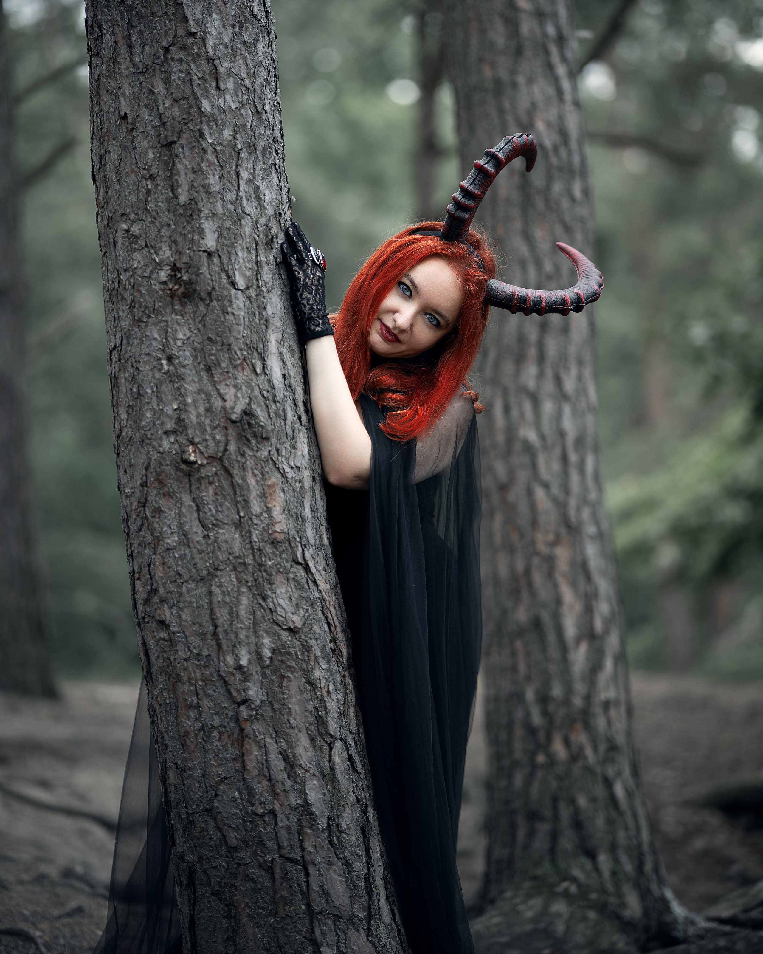 Mystische Szene: Ksenia als Teufelin in schwarzem Mantel zwischen alten Bäumen