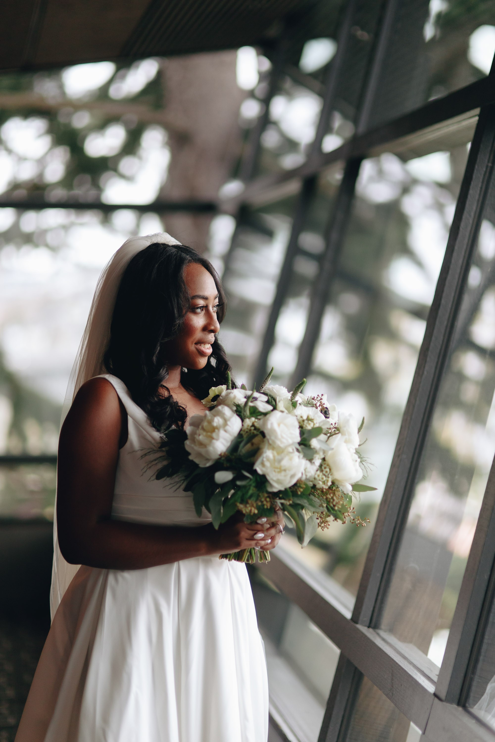 Bride holding bouquet by window, elegant wedding portrait