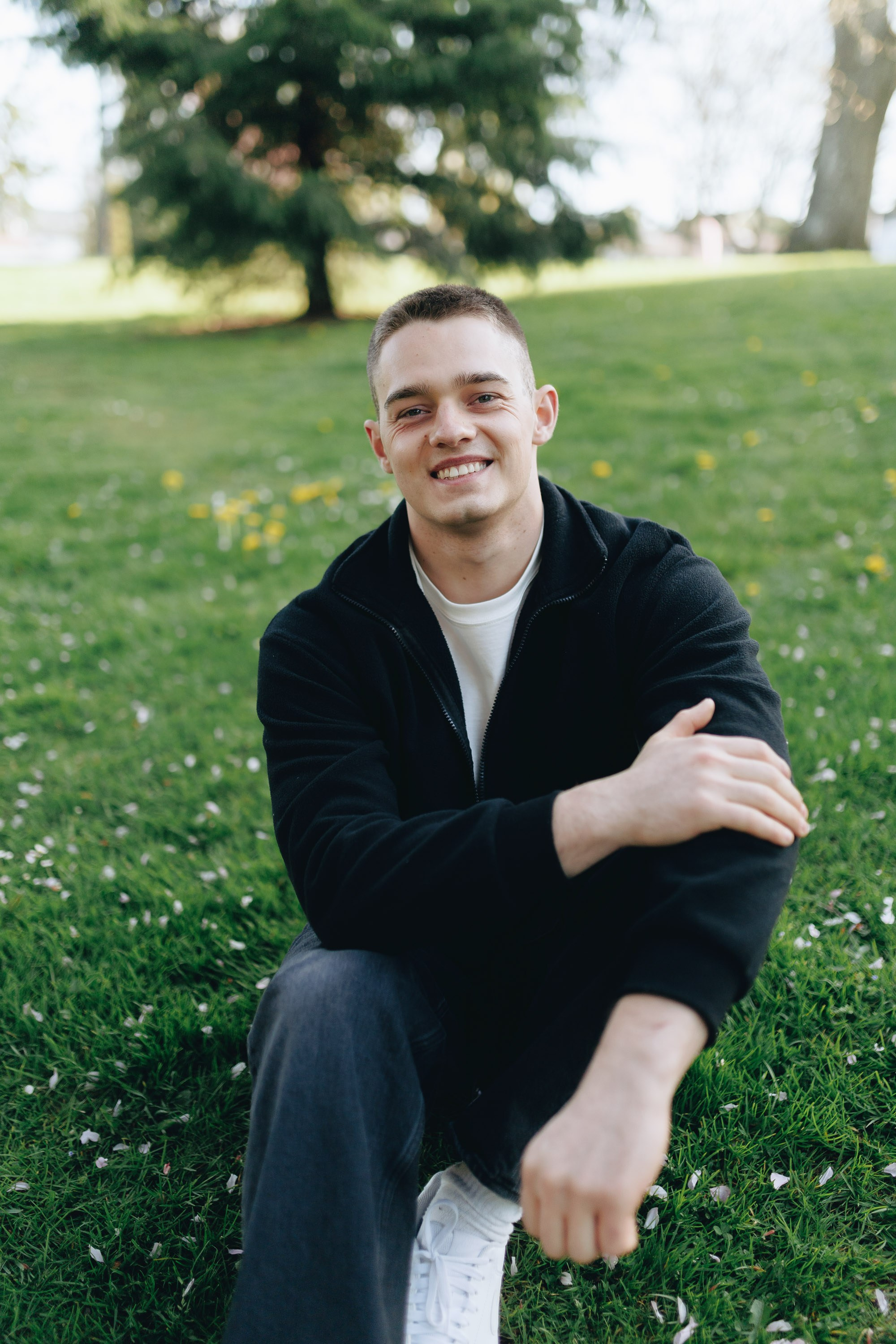 Man in dark sweater sitting on grass, smiling