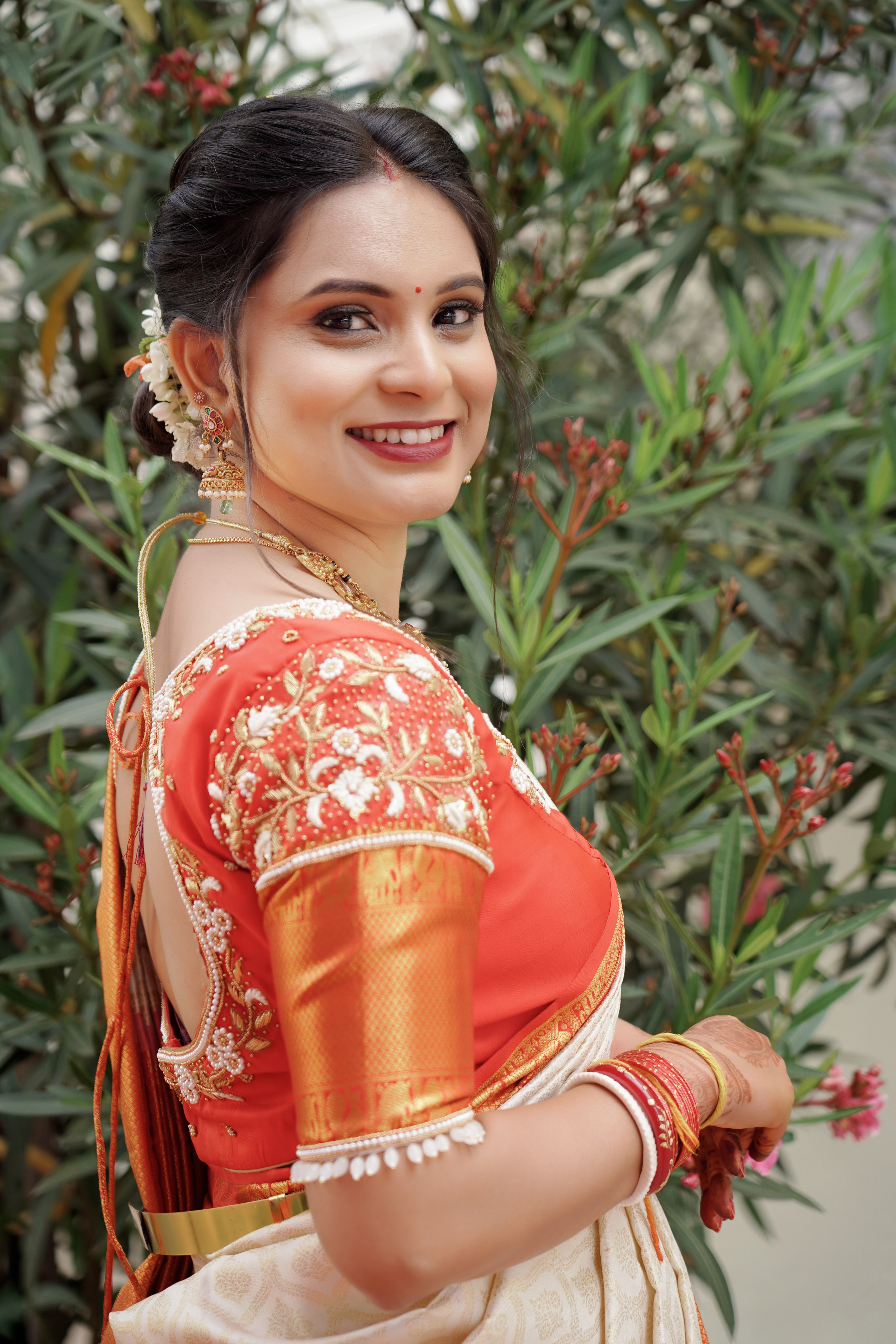 professional portrait of a woman in an orange and white saree and heavily embroidered blouse smiling outdoors in Malleshwaram, Bengaluru