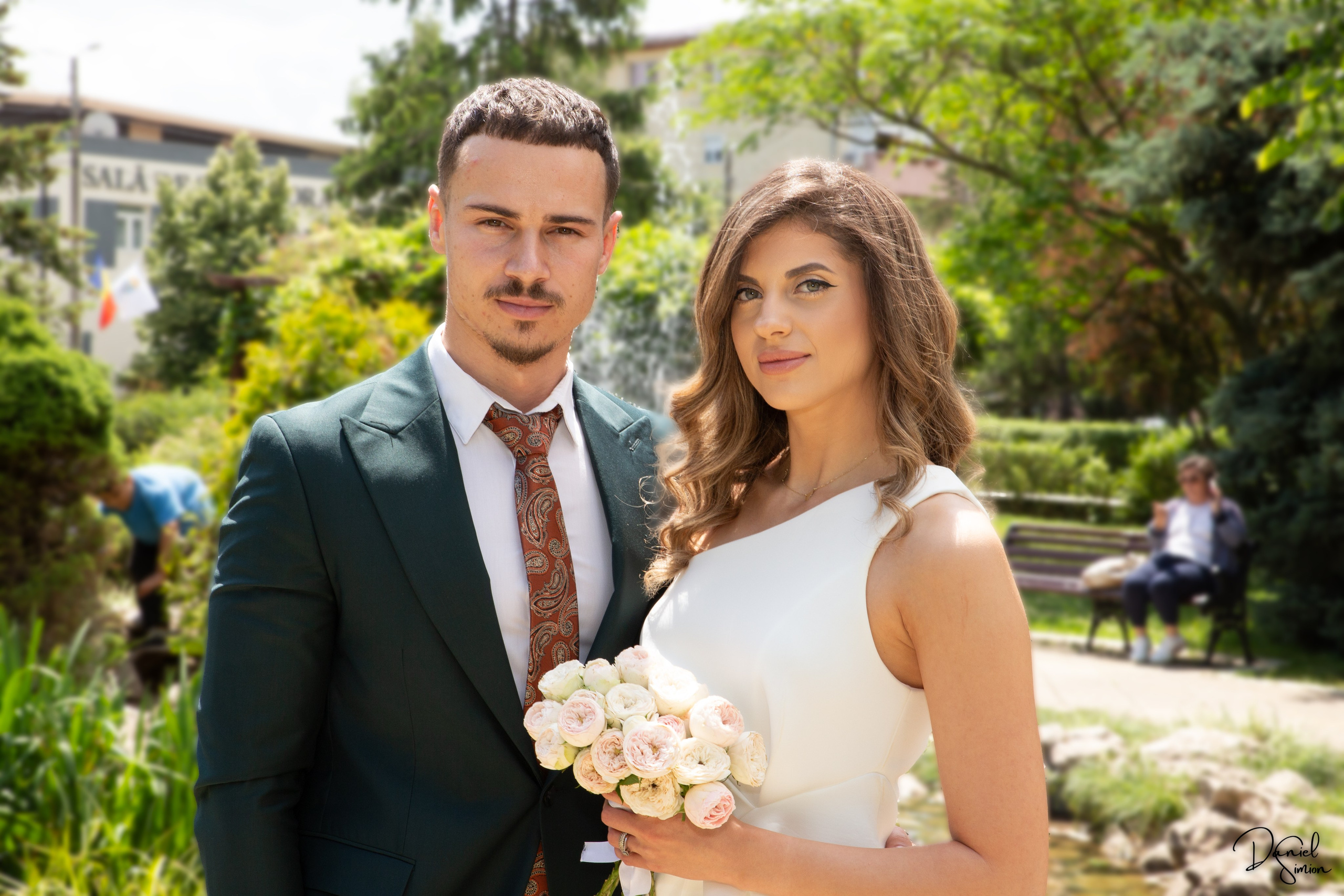 Newlywed couple and two witnesses standing outdoors holding a marriage certificate and bouquets.