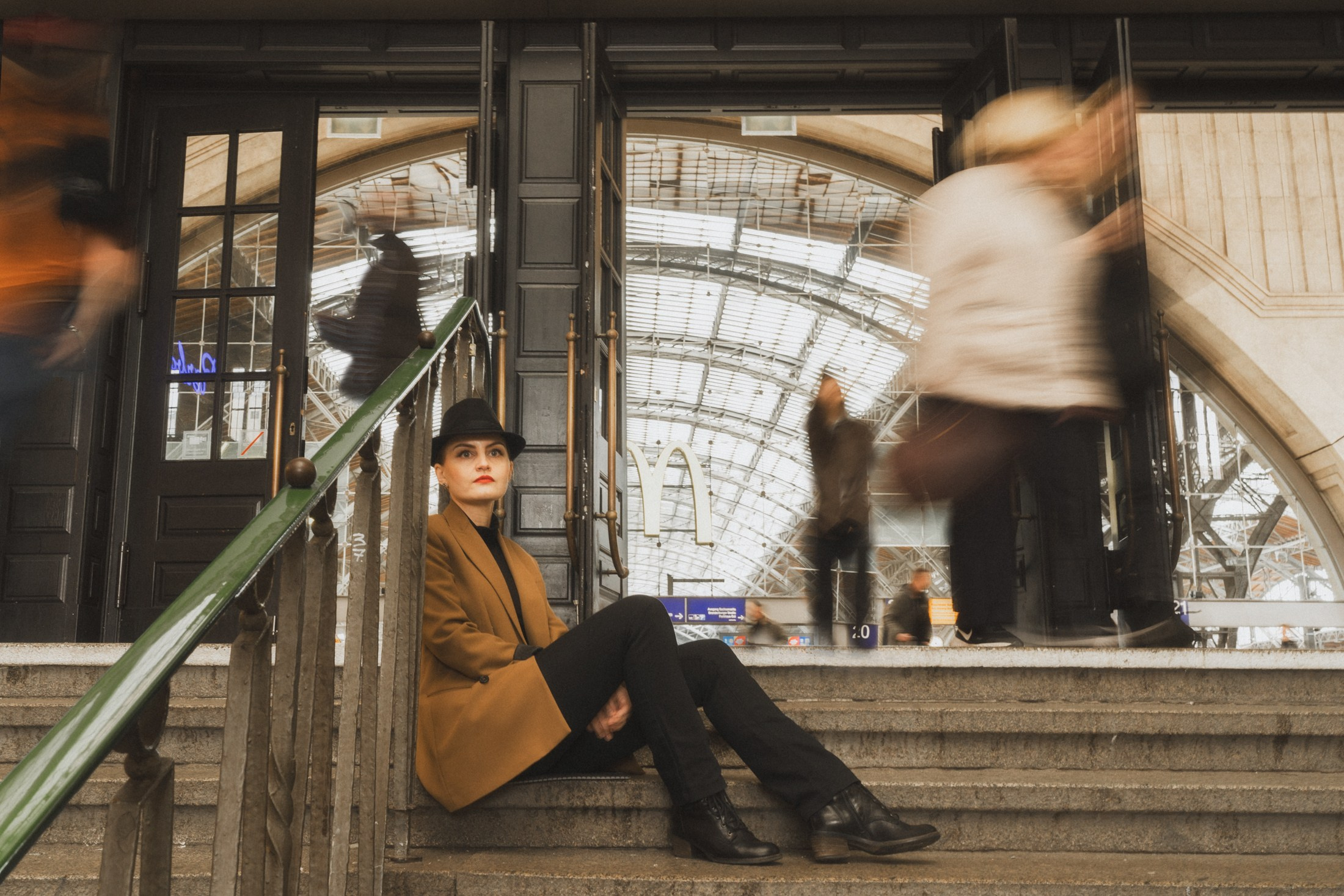 Nachdenkliche Frau sitzt auf der Treppe im Bahnhof, Bewegung der Passanten im Hintergrund