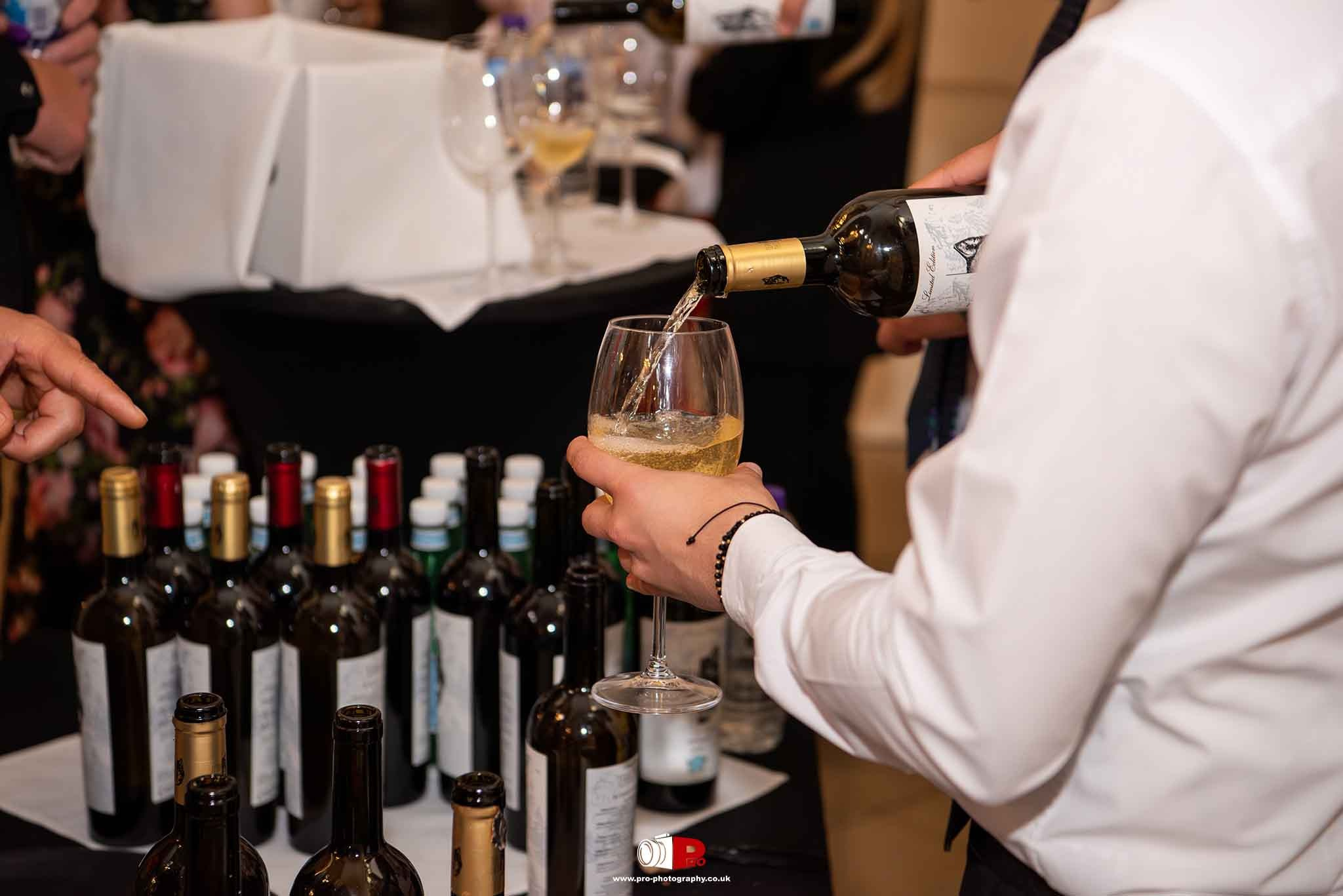 A waiter is pouring white wine into a glass at a stylish wine-tasting reception during a formal event.