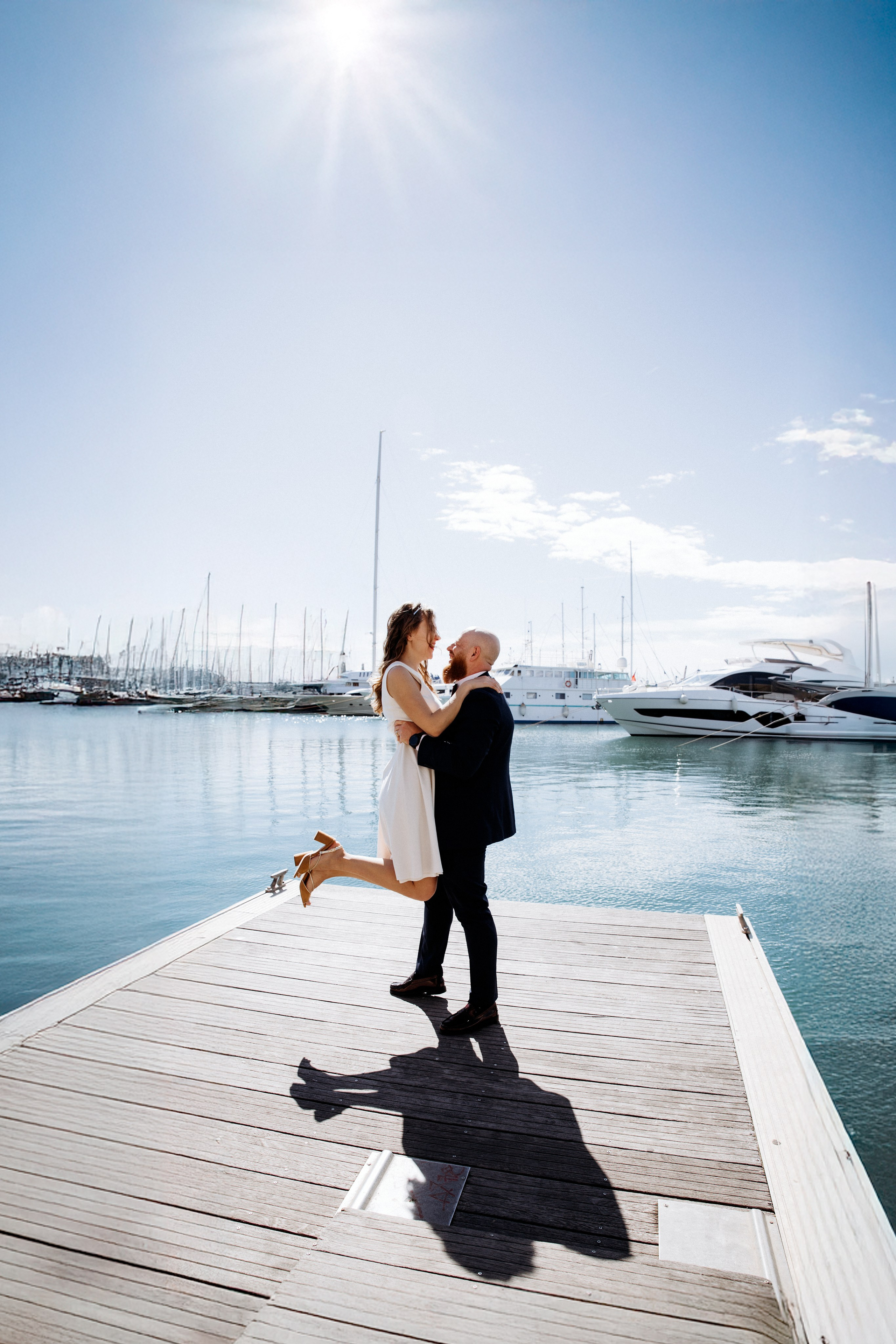 Bride and groom stand together at the end of a dock with calm blue water reflecting their silhouette in València. This modern civil wedding portrait highlights the beauty of a relaxed seaside wedding celebration in Spain.