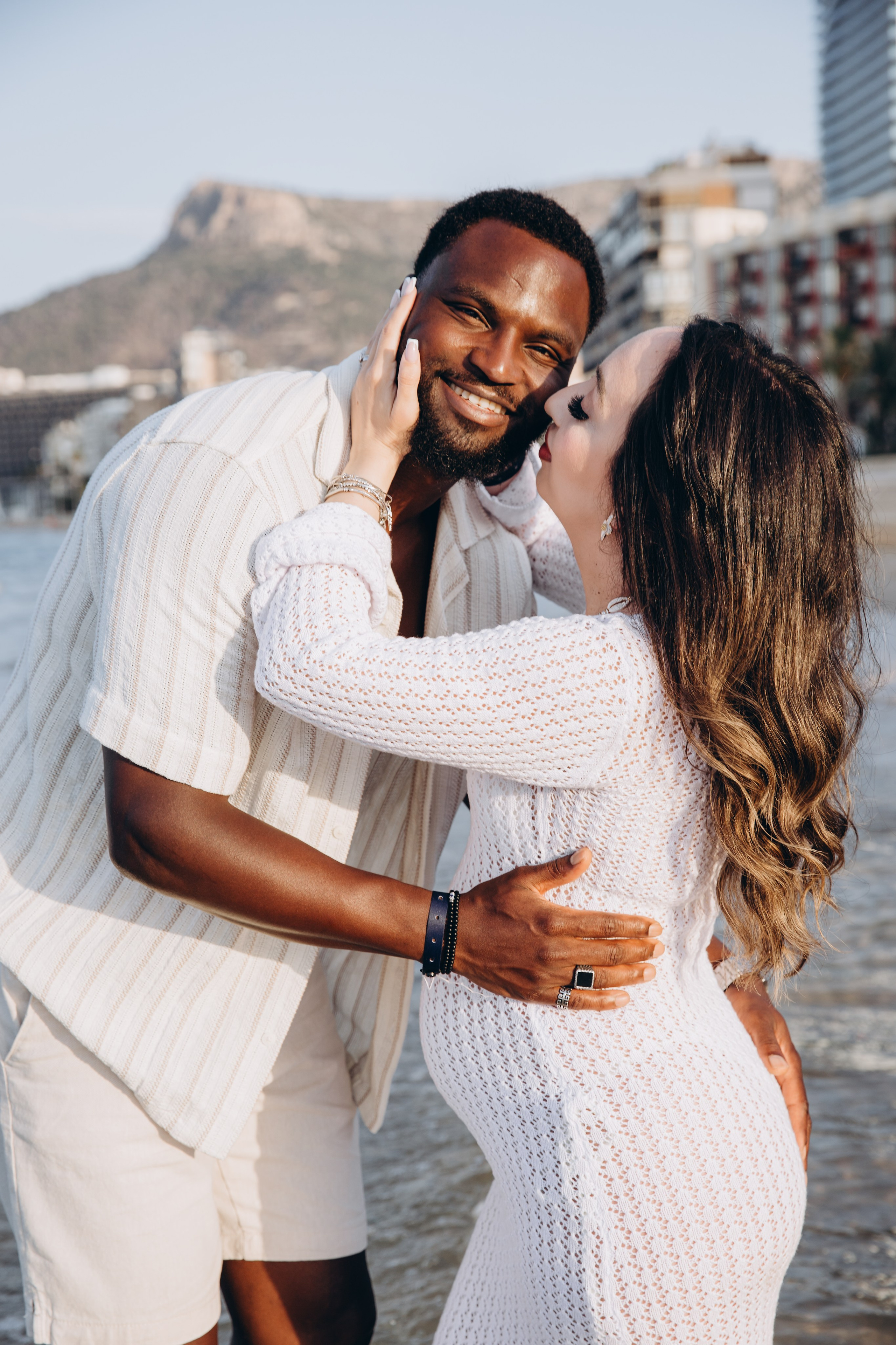 Sesión alegre de embarazo en Benidorm, España — primer plano de una pareja embarazada compartiendo un momento afectuoso junto al mar, capturando amor y expectación.