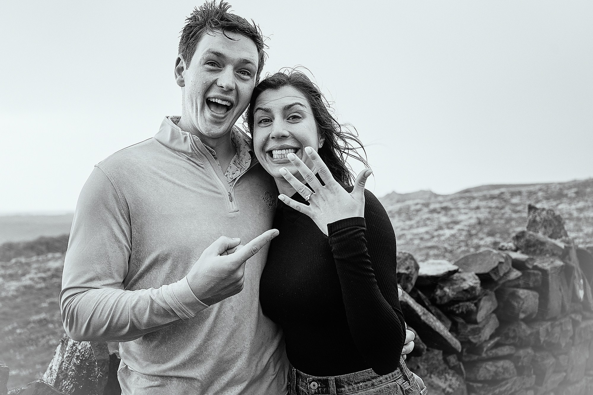Black and white shot of a couple excitedly showing off an engagement ring while overlooking the landscape in County Galway.