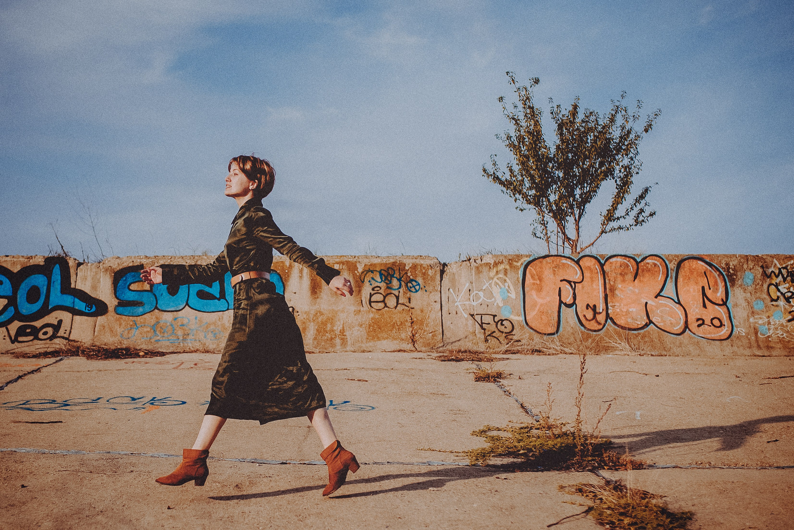 Raluca mergând dinamic în rochie verde lângă zidul cu graffiti în Parcul Văcărești, Photosinteza