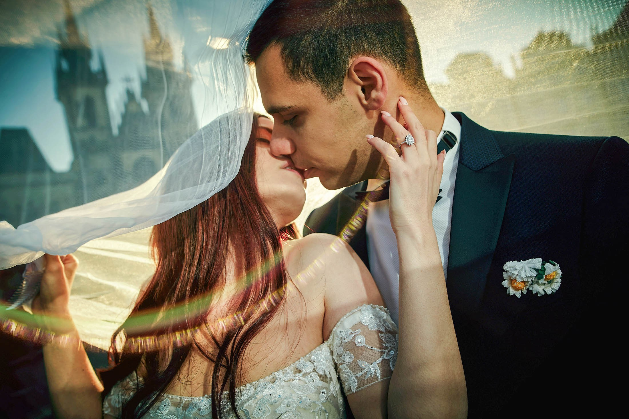The bride and groom kiss under a veil in the Old Town Square in Prague