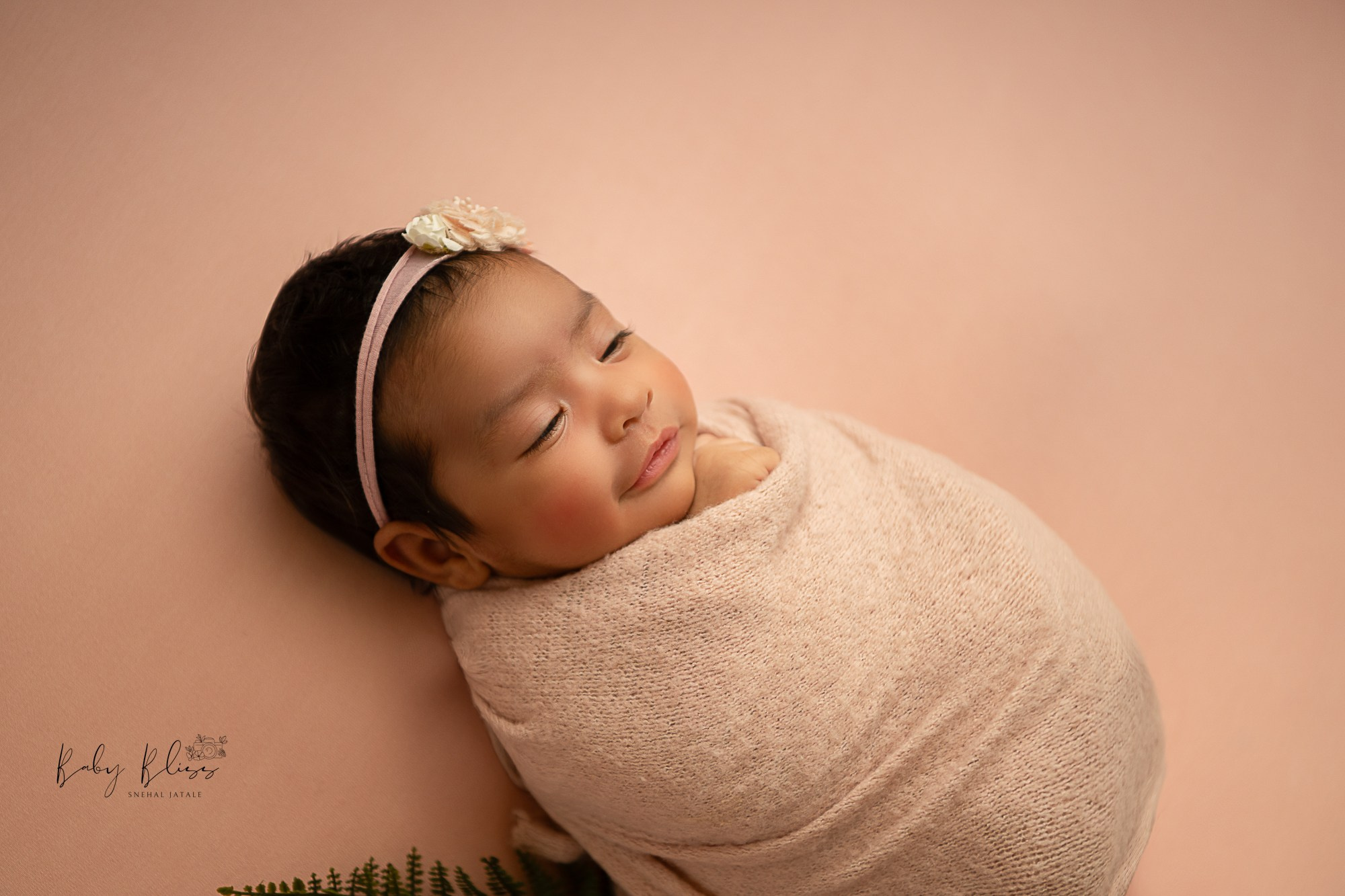 smiling newborn baby girl wrapped in pastel pink wrap.
