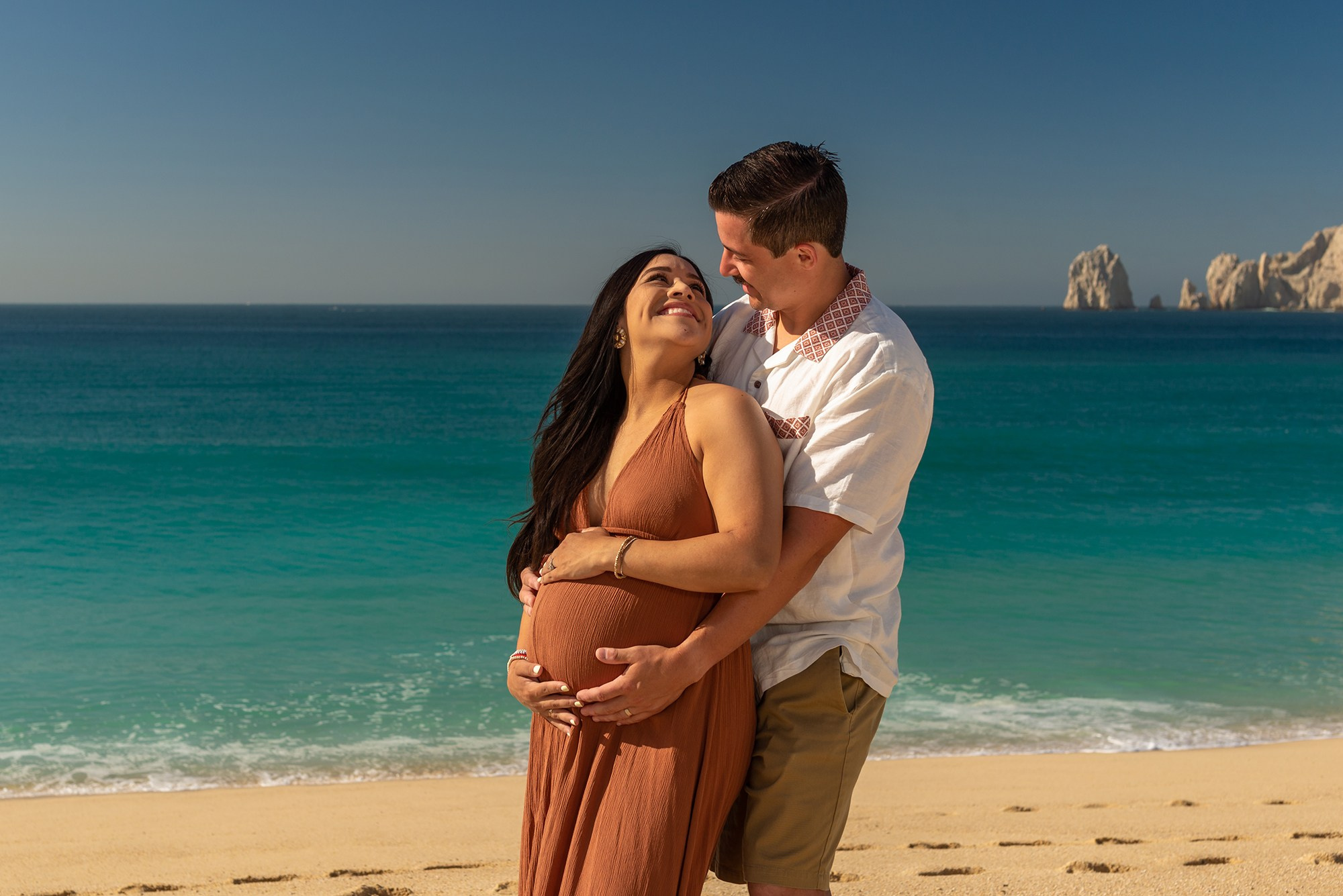 Maternity photography in Baja California Sur – intimate portrait of expecting mother by the sea, hands on her belly, representing love and the miracle of life