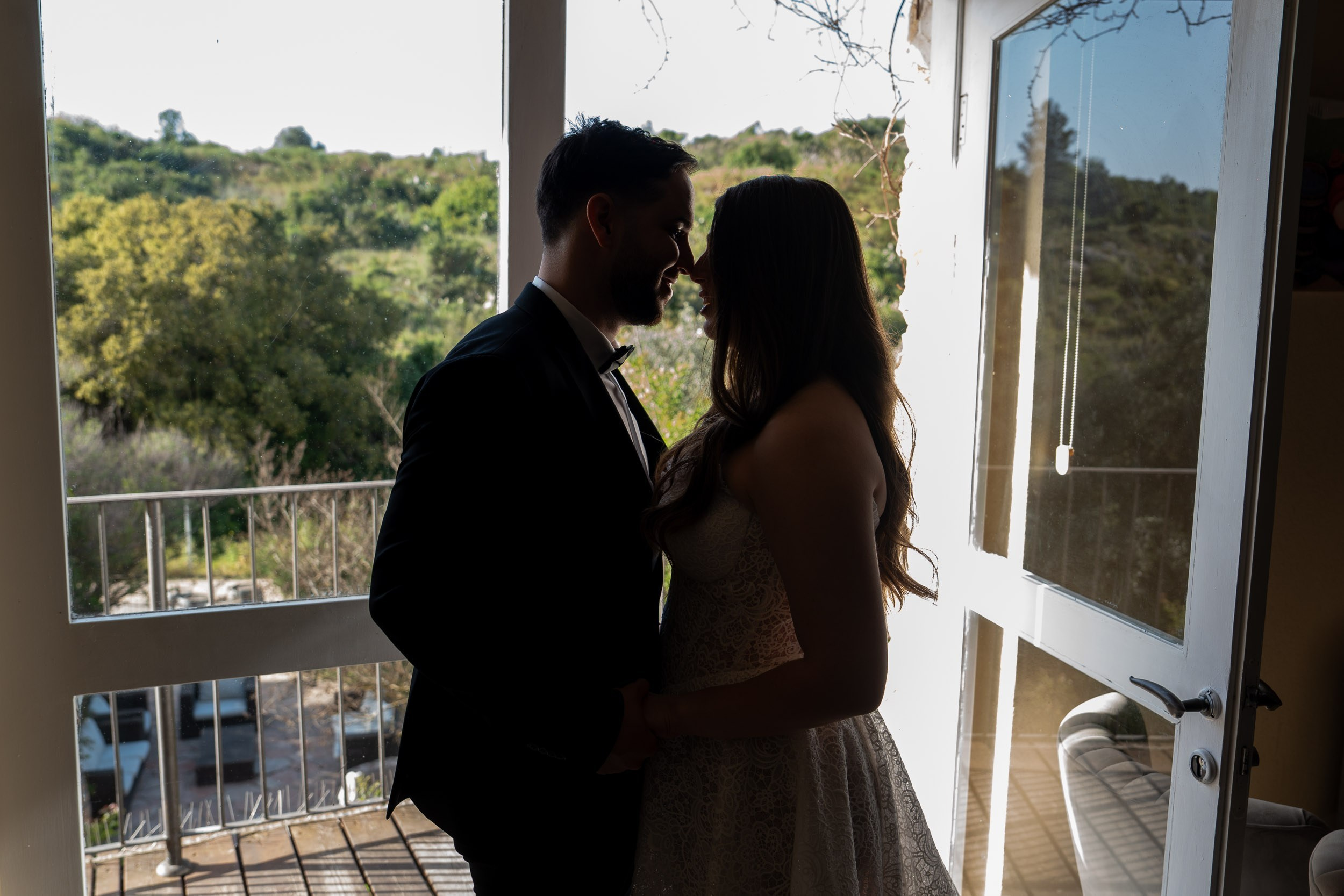 A bride and groom share a quiet moment in silhouette beside a window