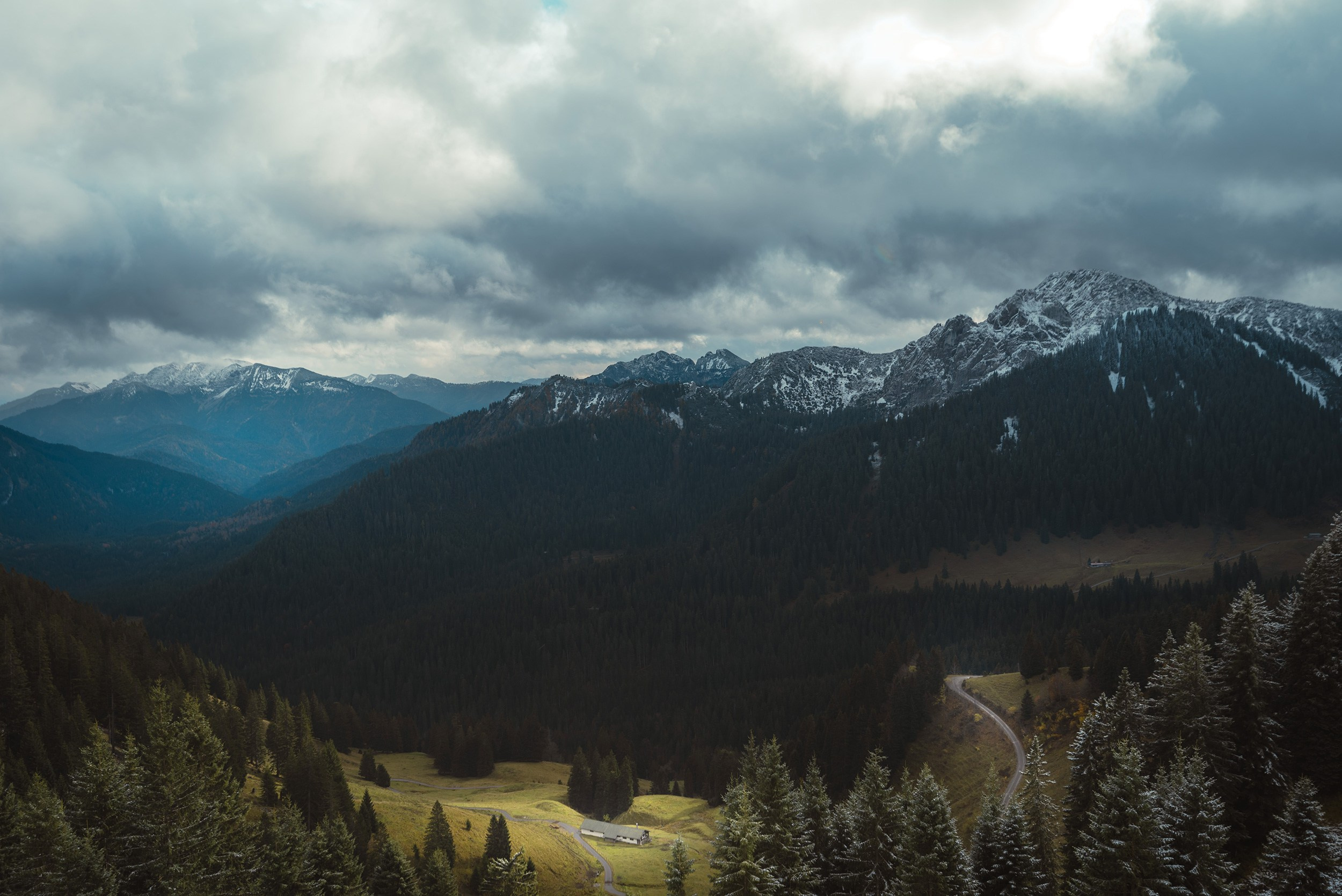 View of alpine ridges and dark forests from Wallberg under heavy, overcast clouds.