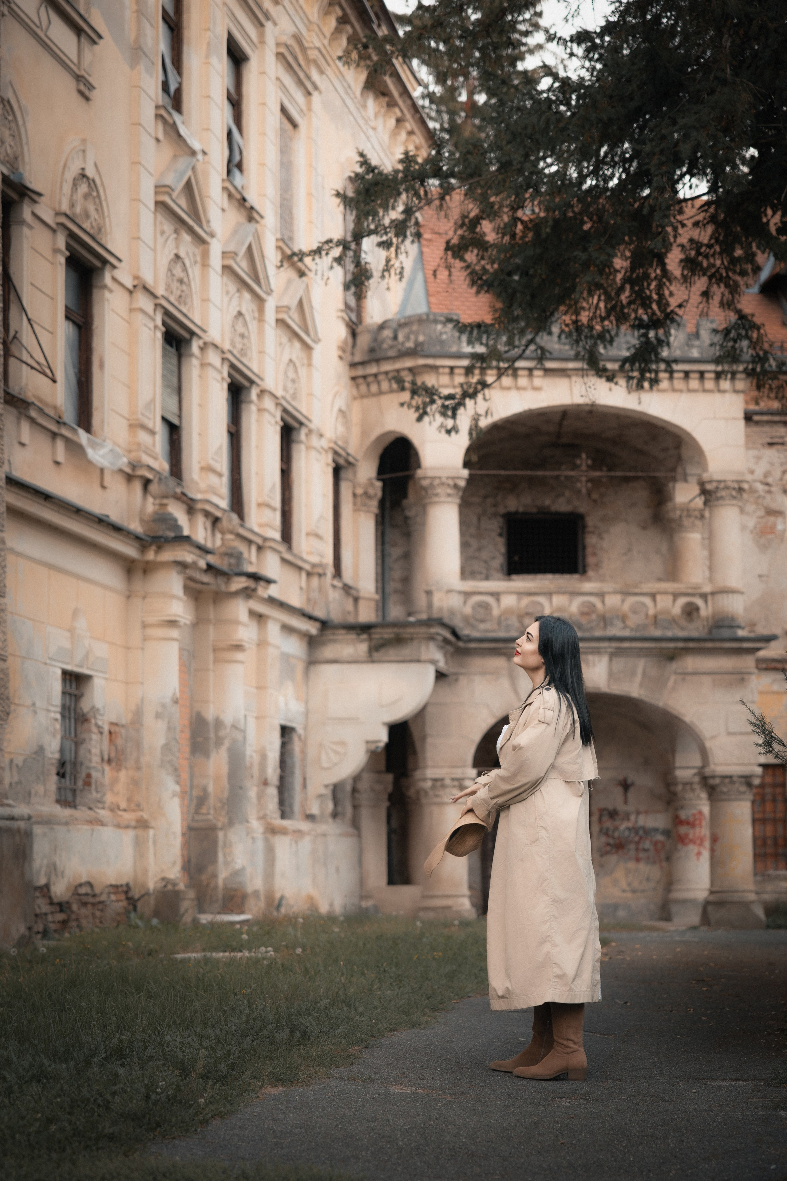 Ženska v klobuku pred dvorcem Viltuš. Fotografija prikazuje prefinjeno gradacijo svetlobe s prehodom iz mehkih osvetljenih delov v globoke mat sence, kar poudari teksturo kamna.4