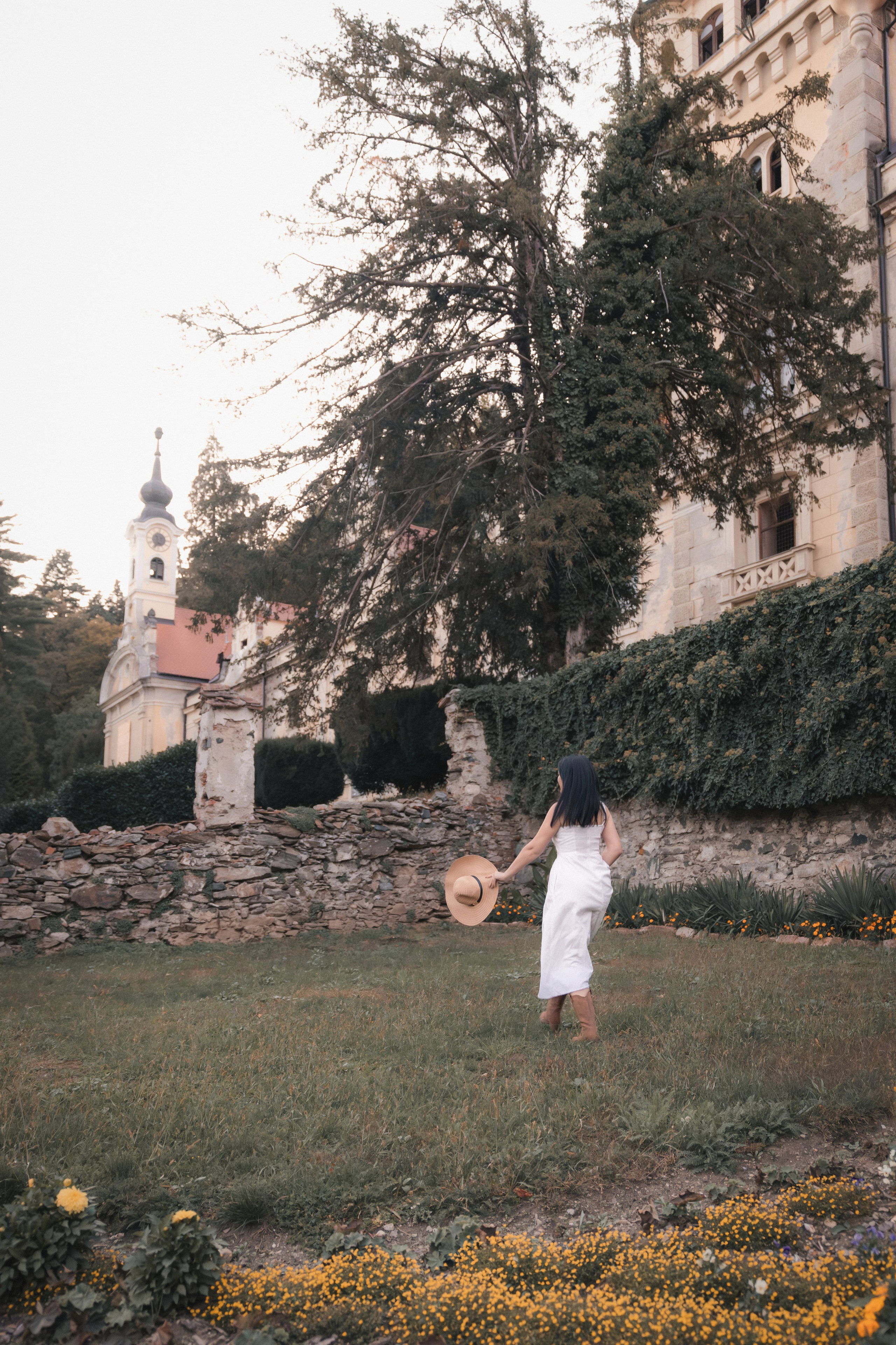 Ženska v klobuku pred dvorcem Viltuš. Fotografija prikazuje prefinjeno gradacijo svetlobe s prehodom iz mehkih osvetljenih delov v globoke mat sence, kar poudari teksturo kamna.188