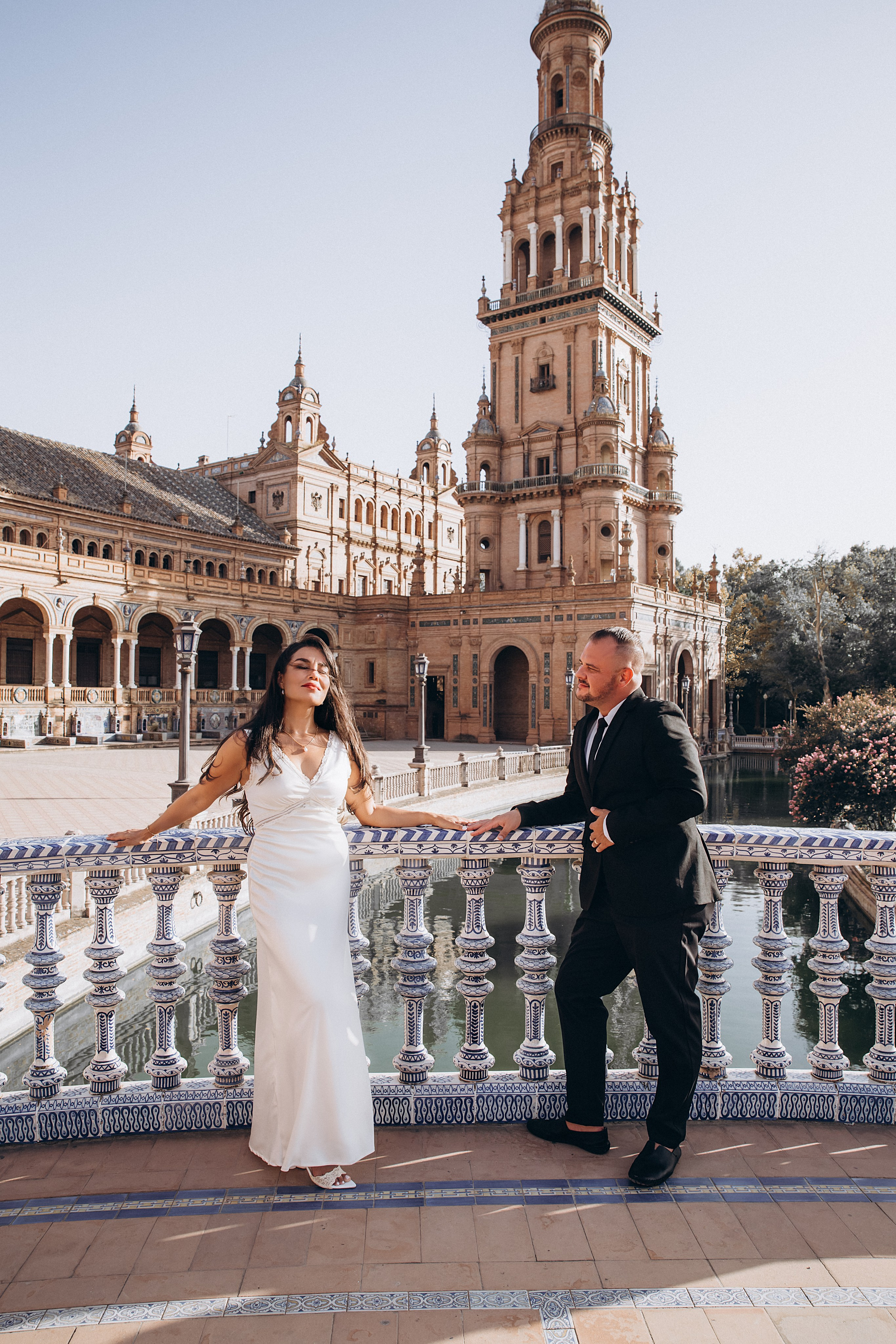 Romantic wedding photo at Plaza de España in Sevilla, Spain, featuring a joyful bride and groom by the ornate blue-and-white bridge, perfect for couples searching for elegant and timeless wedding photoshoots in Seville or destination wedding photography in Spain.