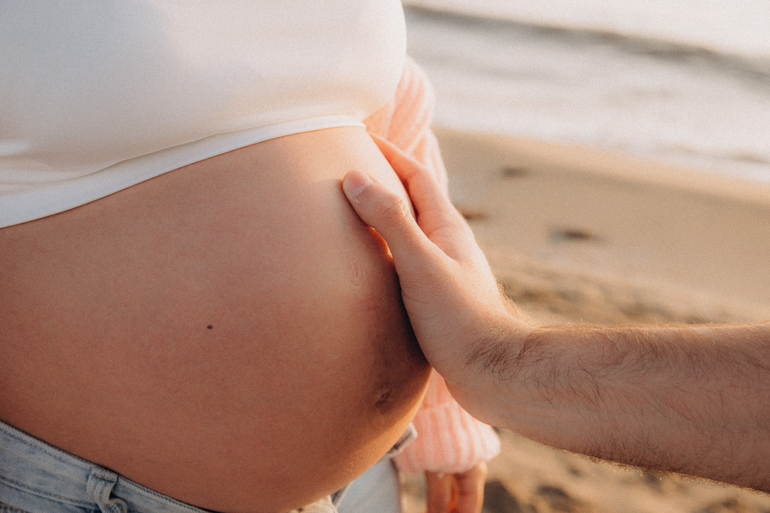 Sesión de fotos de embarazo en Valencia, España, con un primer plano de una barriga de embarazada con manos acariciándola suavemente, capturada con luz natural suave para un detalle íntimo y emocional — ideal para sesiones de embarazo y maternity en Valencia y en toda España.