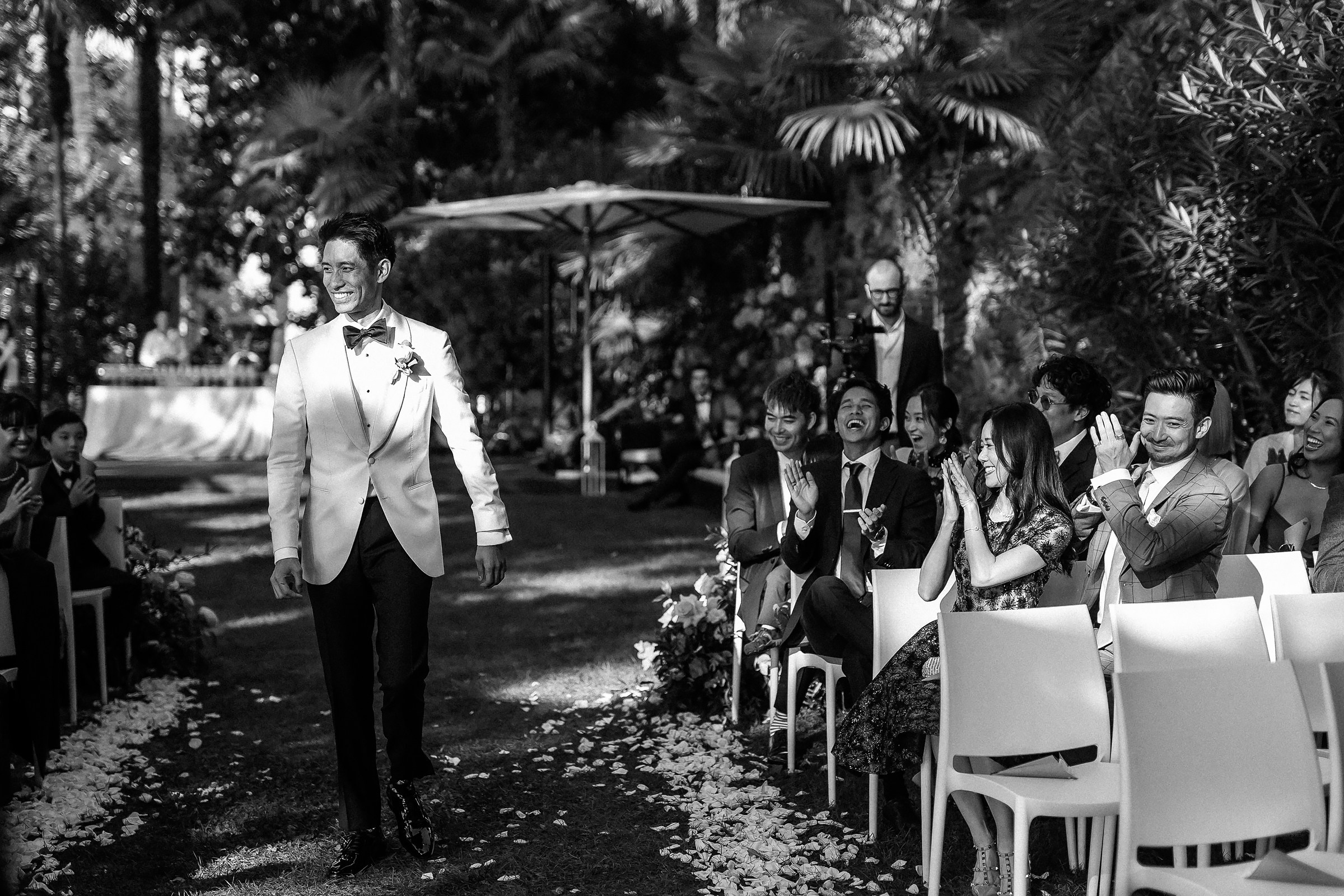 Groom smiles as he walks down the aisle, with guests applauding on both sides.