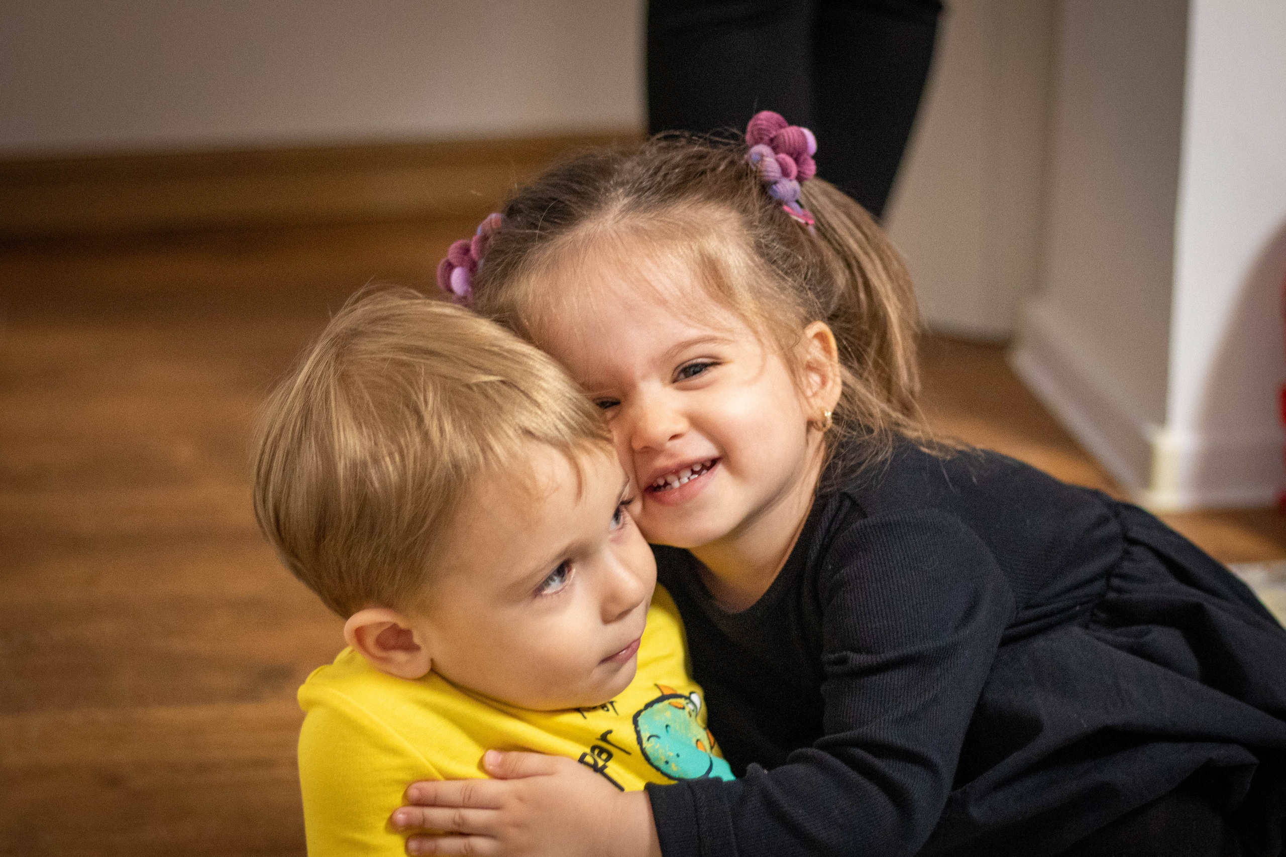 Small child hugging another child affectionately on a living room sofa.