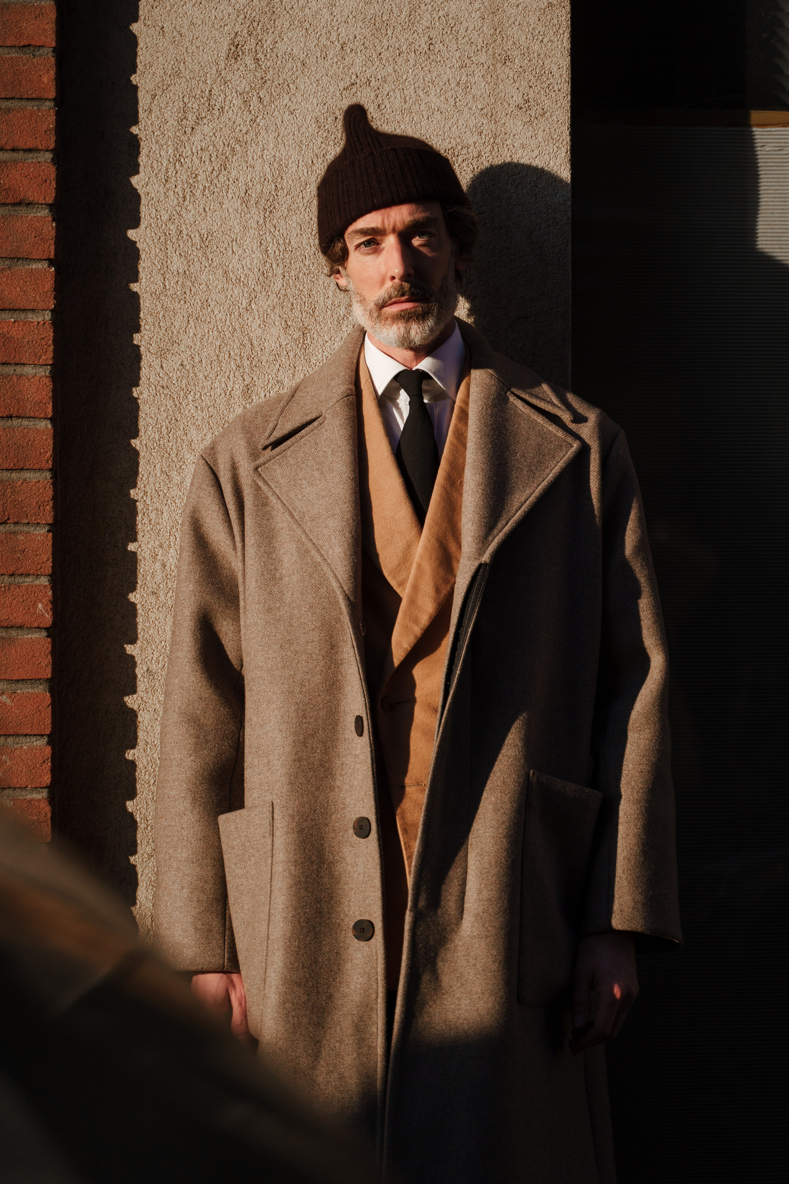 Stylish gentleman in classic overcoat and beanie at Milan Fashion Week captured by a Milanese photographer