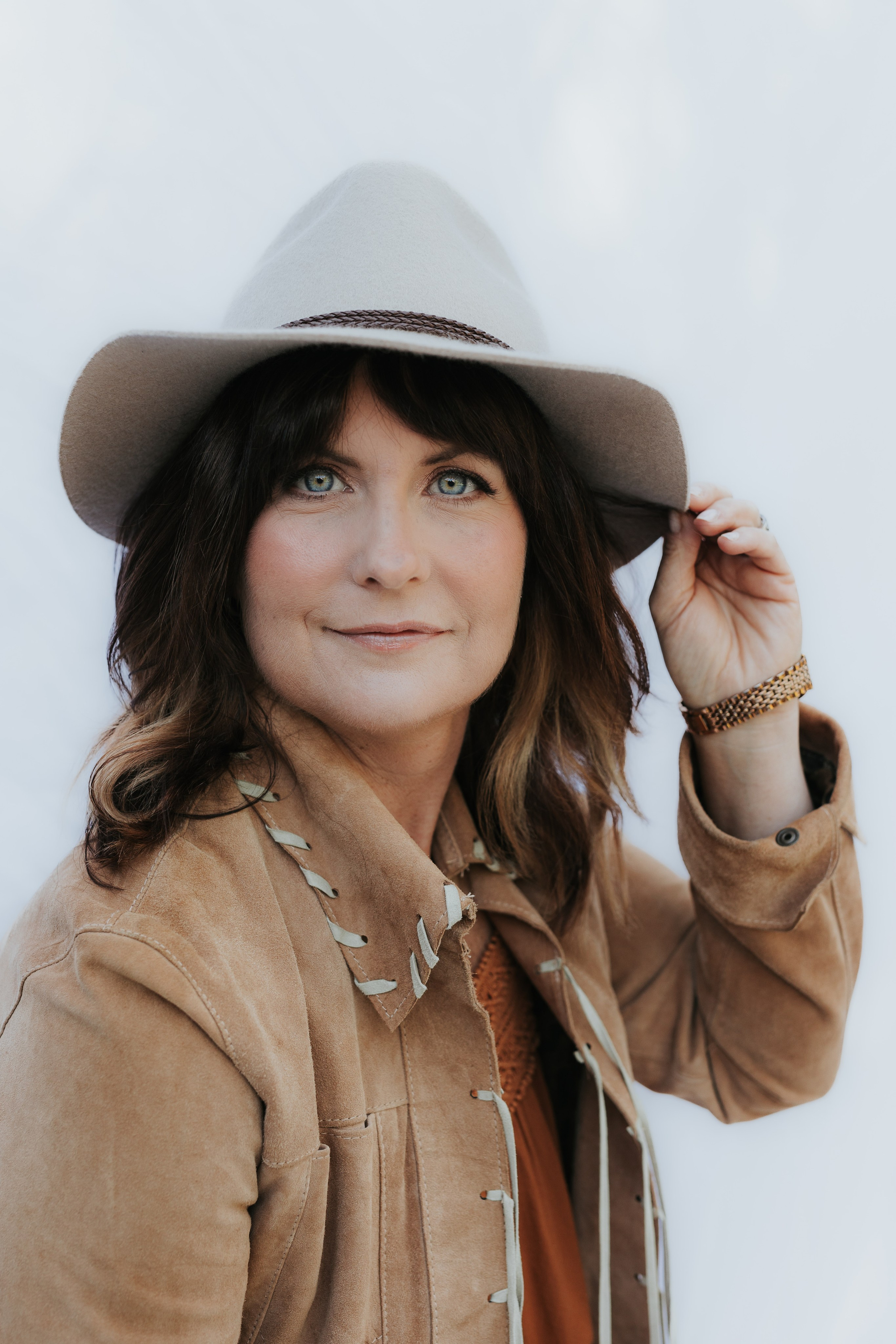 headshot of a woman wearing a cowboy hat, brown jacket with bright blue eyes 