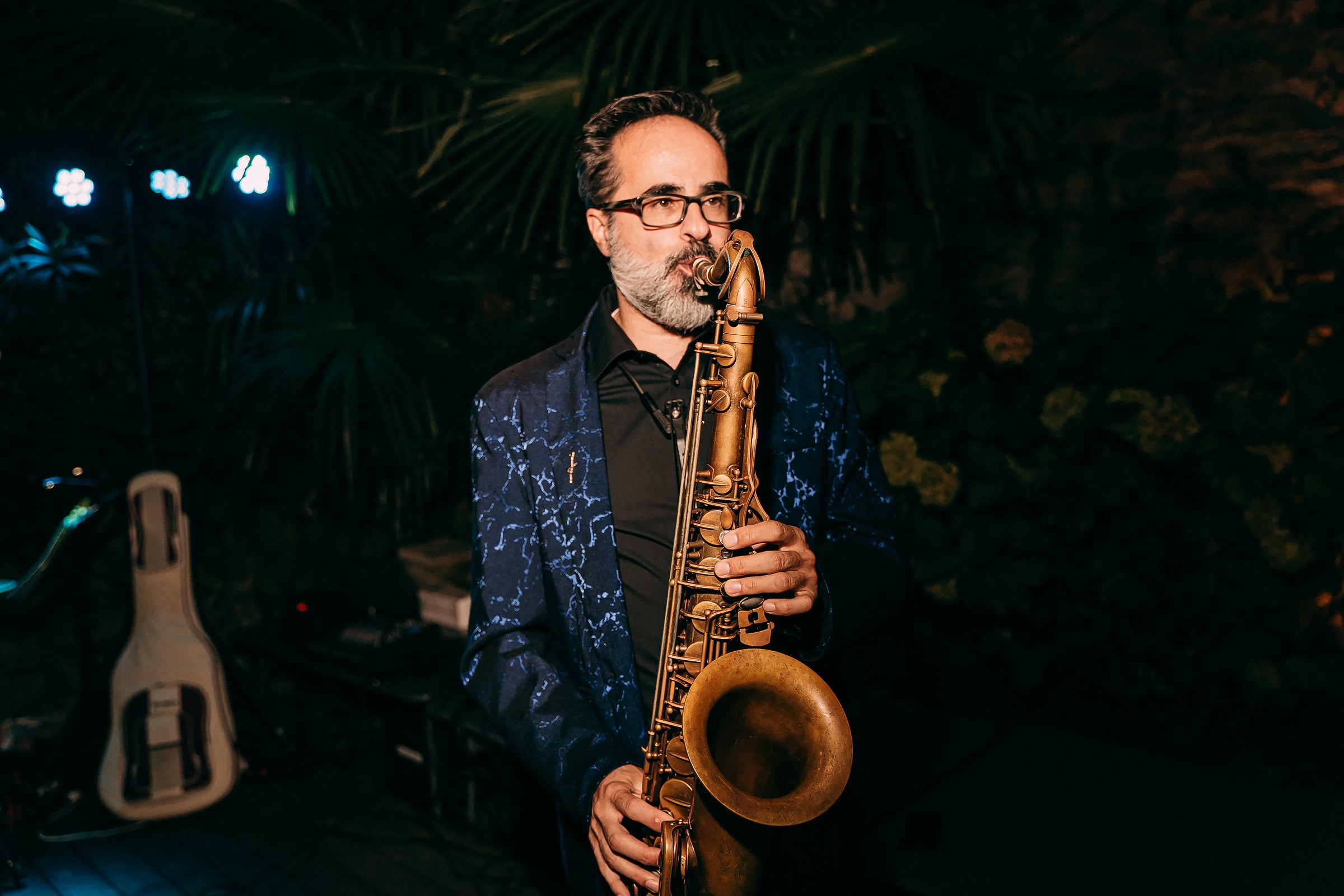 Jazz musician passionately playing the saxophone, dressed in a blue suit, under soft evening lights at the event.