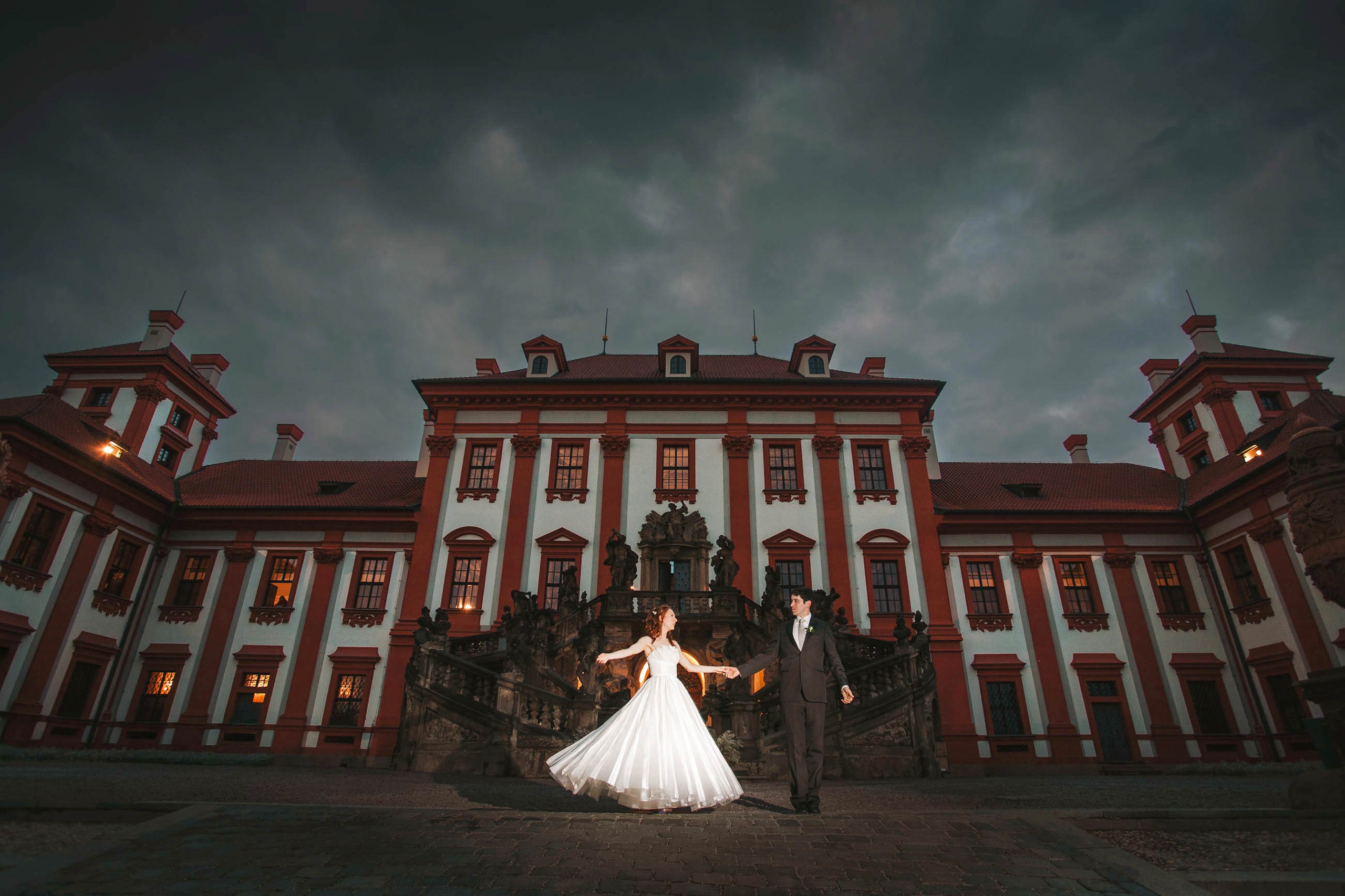 Newlyweds practice their first dance under the night sky in front of the historic Troja Palace on their wedding day.