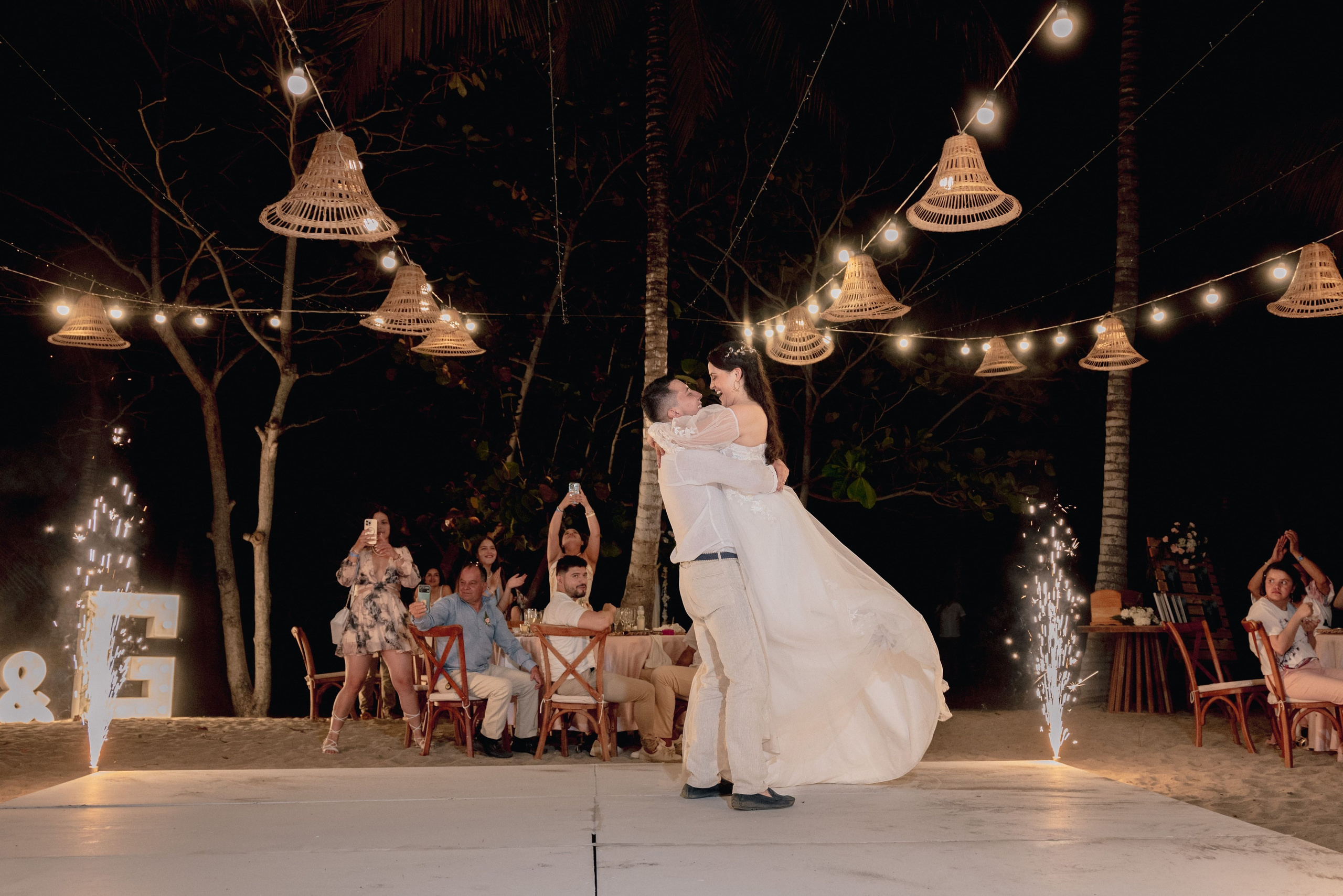 Celebración nocturna con iluminación en boda de playa, momento de alegría entre pareja e invitados